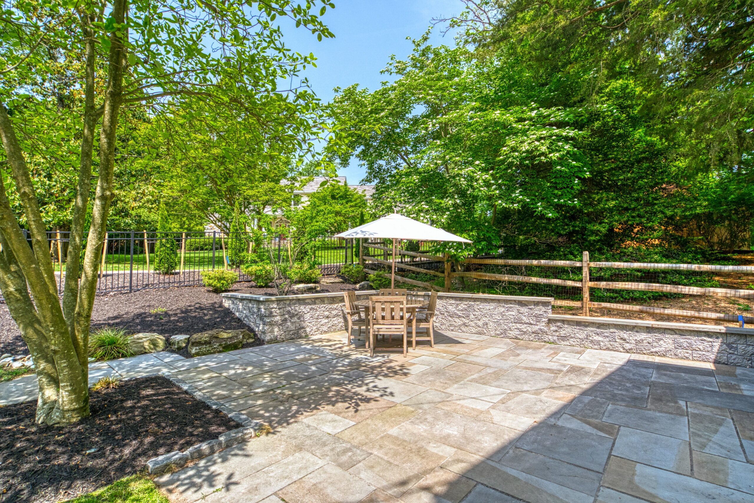 Professional exterior photo of 209 Norwood Road, Annapolis, MD - showing the flag stone patio with retaining wall, fence, and landscaping and patio furniture with umbrella