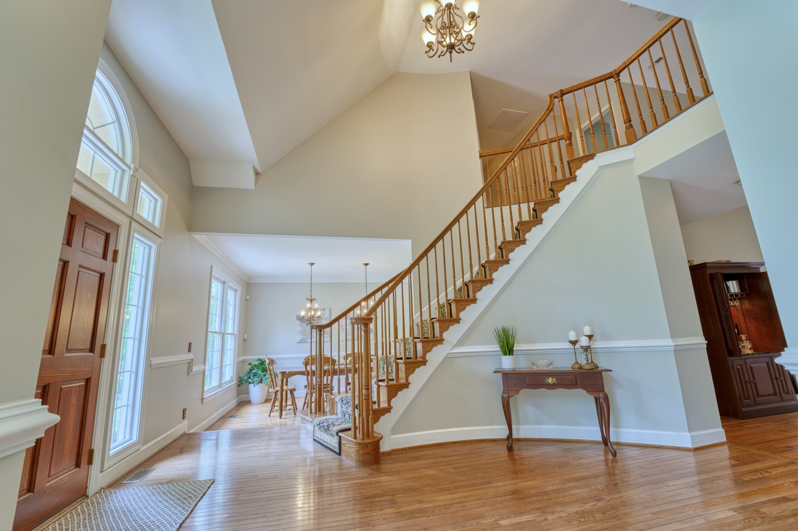 Professional interior photo of 13700 Holly Forest Dr - showing the entry hall with 2-story vaulted ceiling, hardwood floors and a curving staircase to the upstairs catwalk.