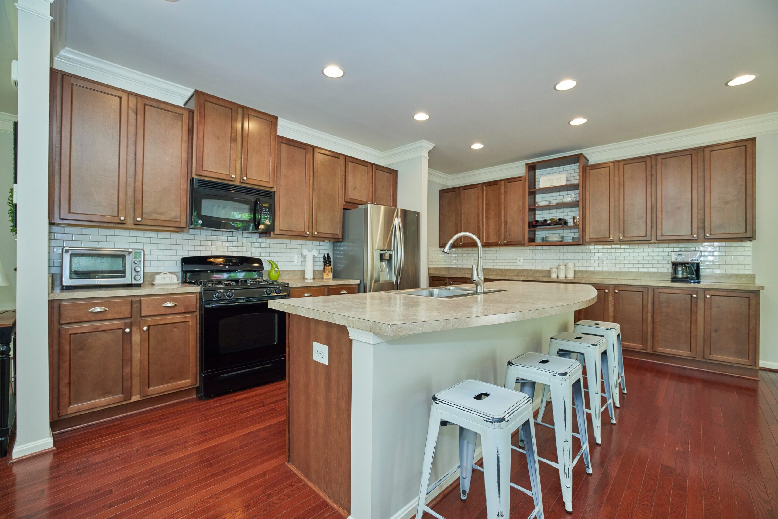 Professional interior photo of 12030 Lake Dorian Drive, Bristow, VA - showing the kitchen with dark wooden cabinets, black range, stainless fridge and large island with sink