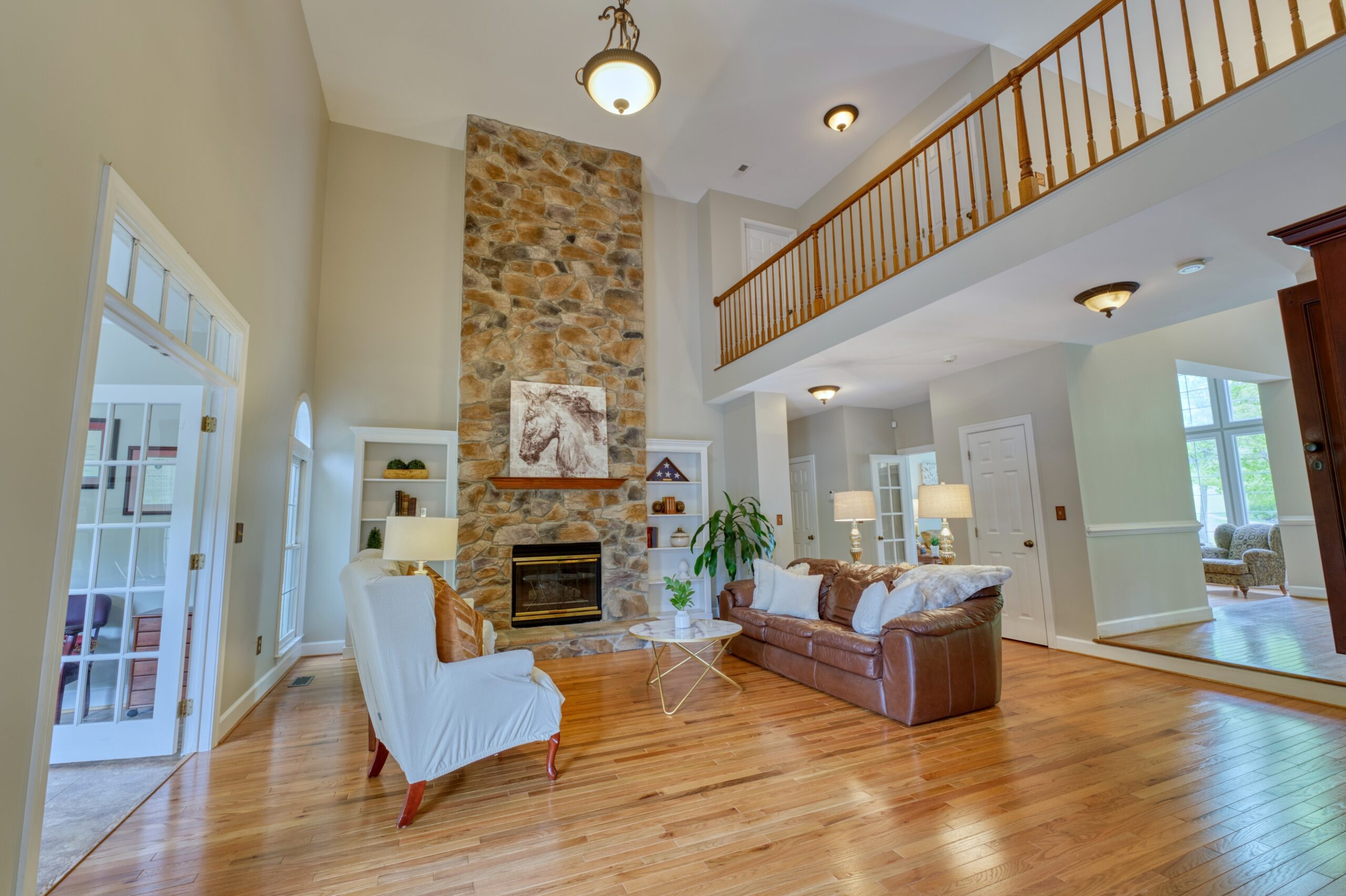 Professional interior photo of 13700 Holly Forest Dr - showing the main living room with hardwood floors, looking away from the windows toward the 2-story stone fireplace flanked by white built-in bookshelves
