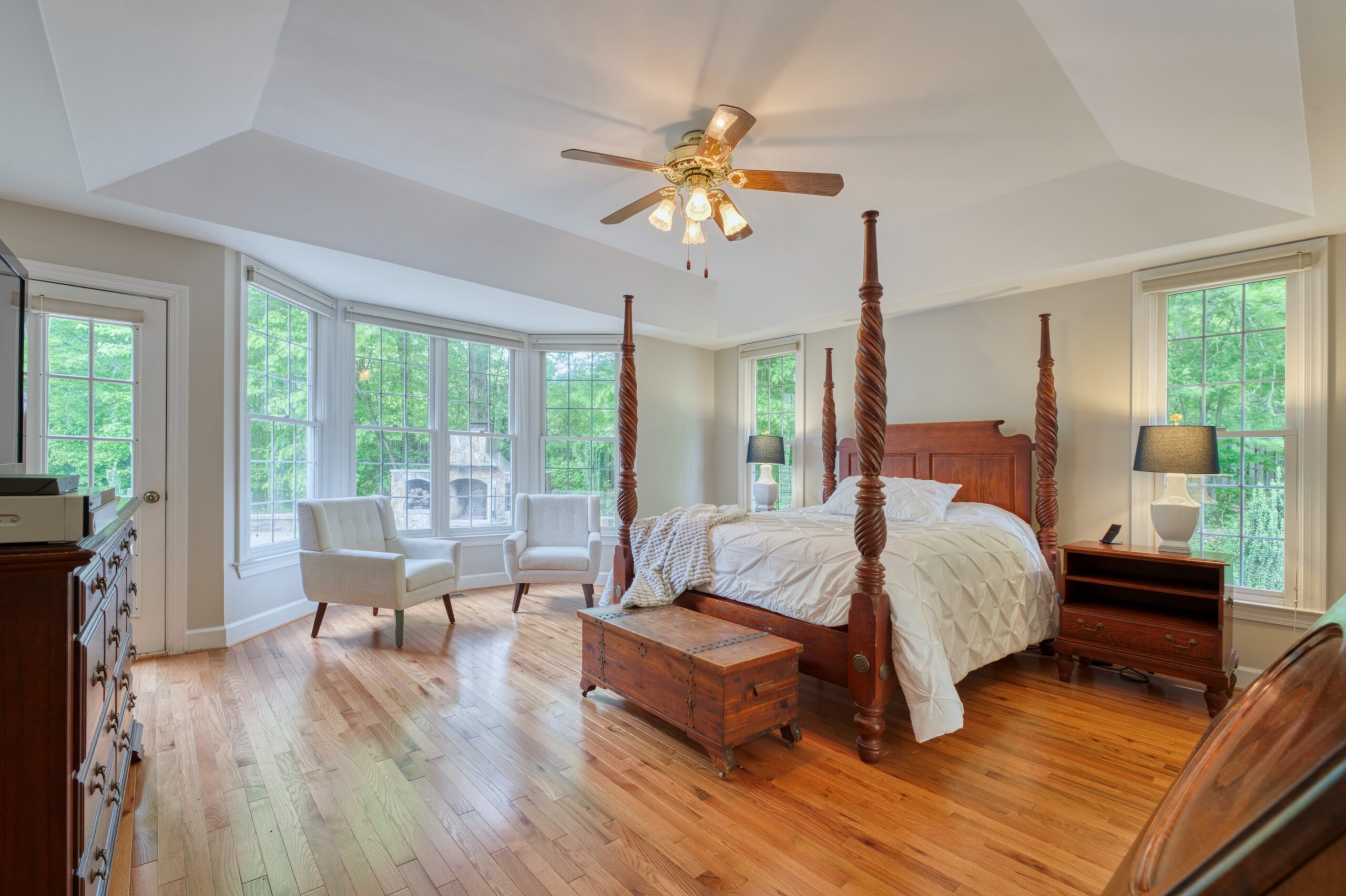 Professional interior photo of 13700 Holly Forest Dr - showing the master bedroom with deep tray ceiling and ceiling fan, hardwood floors, lots of windows and a door out the private patio