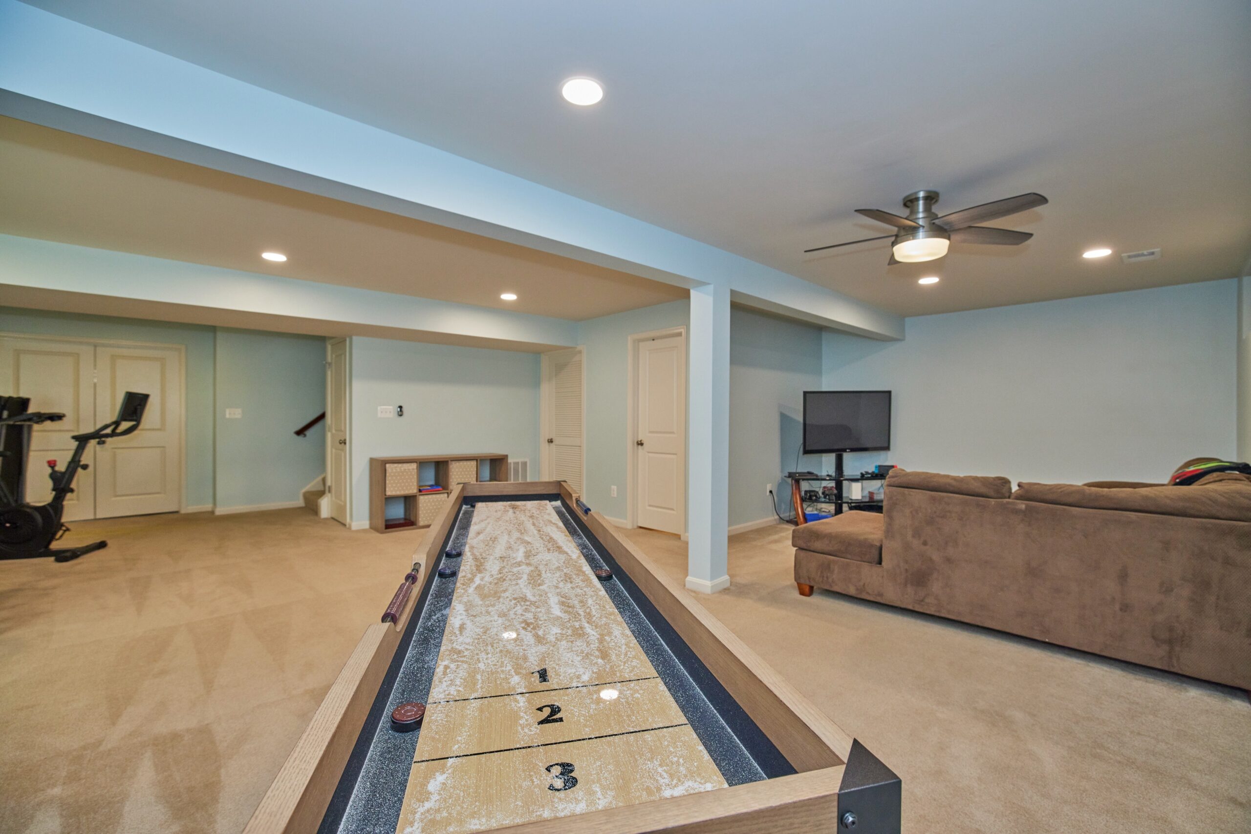 Professional interior photo of 12030 Lake Dorian Drive, Bristow, VA - showing the basement with cream carpeting, light blue walls and furniture with a shuffleboard table