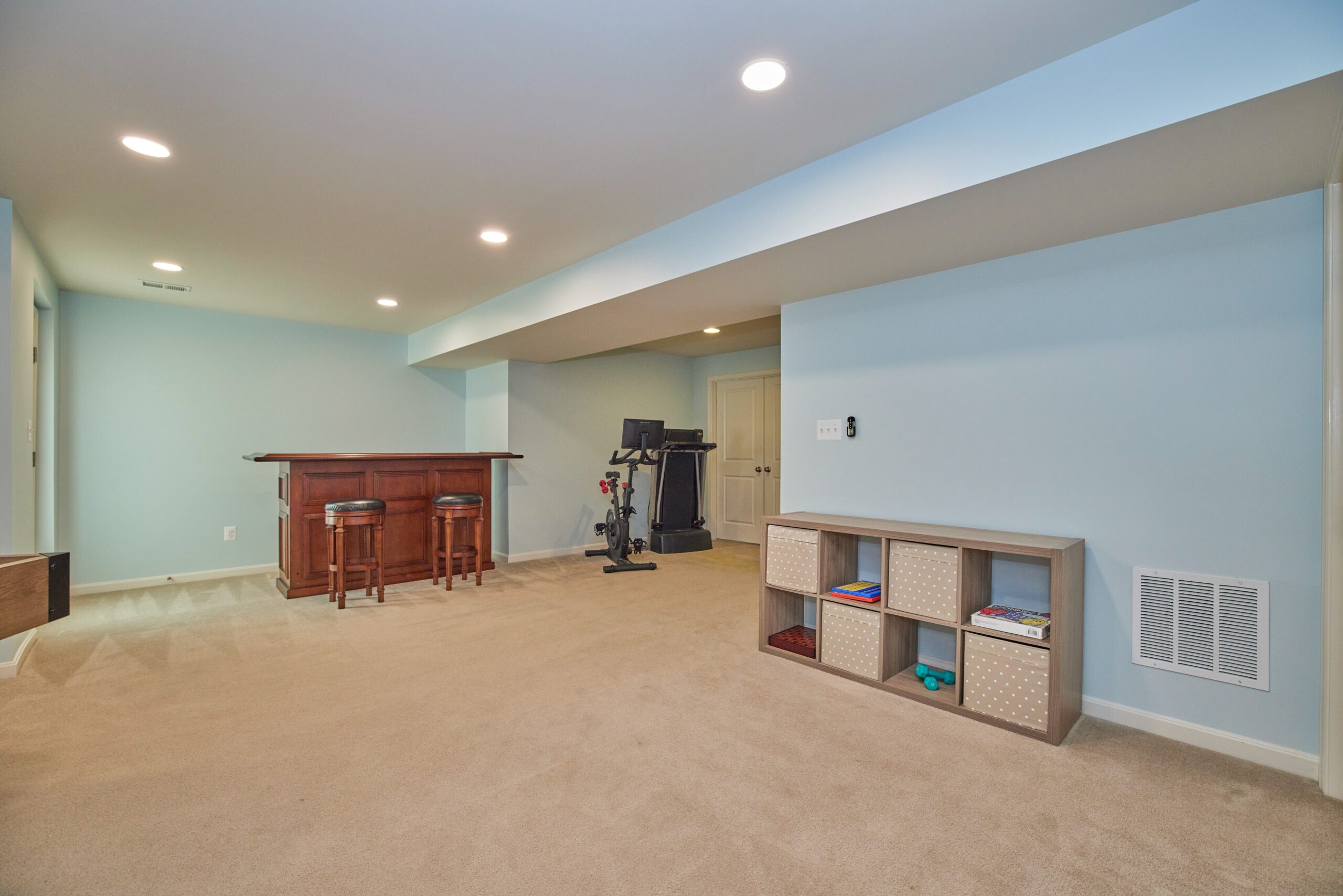 Professional interior photo of 12030 Lake Dorian Drive, Bristow, VA - showing the basement with cream carpeting, light blue walls and a built in oak bar in the background
