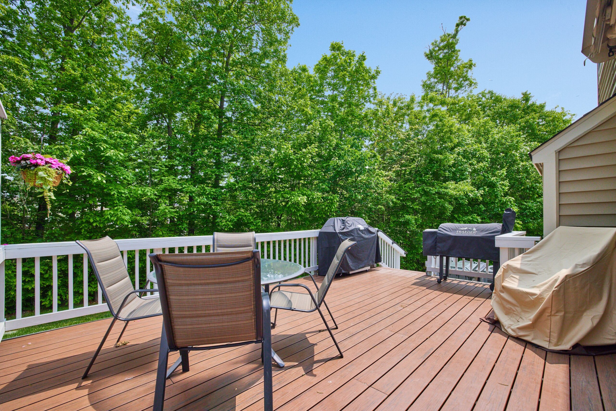Professional exterior photo of 12030 Lake Dorian Drive, Bristow, VA - showing the large rear deck with patio furniture and 2 grills and green tree buffer beyond