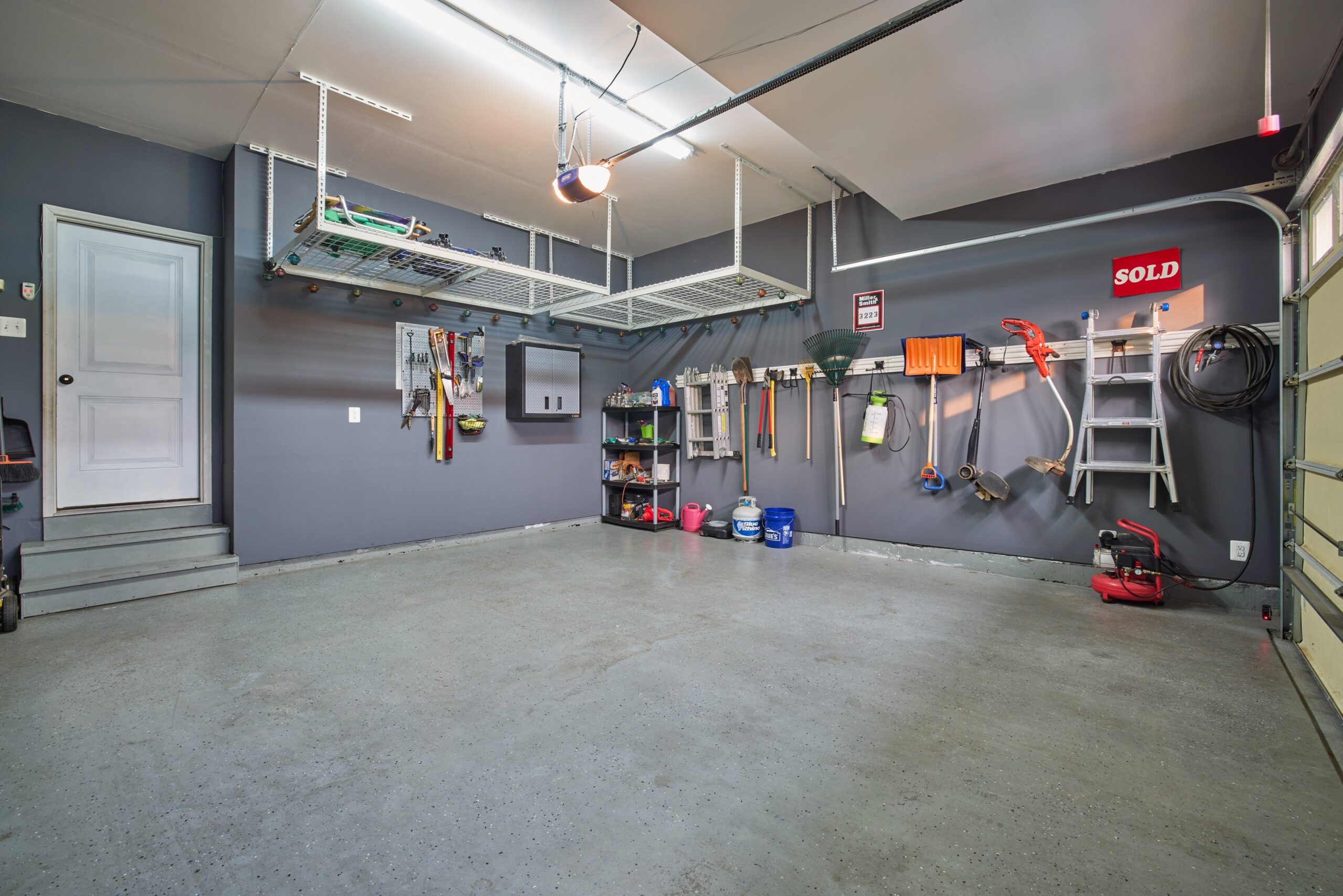 Professional interior photo of 12030 Lake Dorian Drive, Bristow, VA - showing the inside of a 2-car garage, perfectly clean with wall racks for hanging large tools and ceiling racks for additional storage