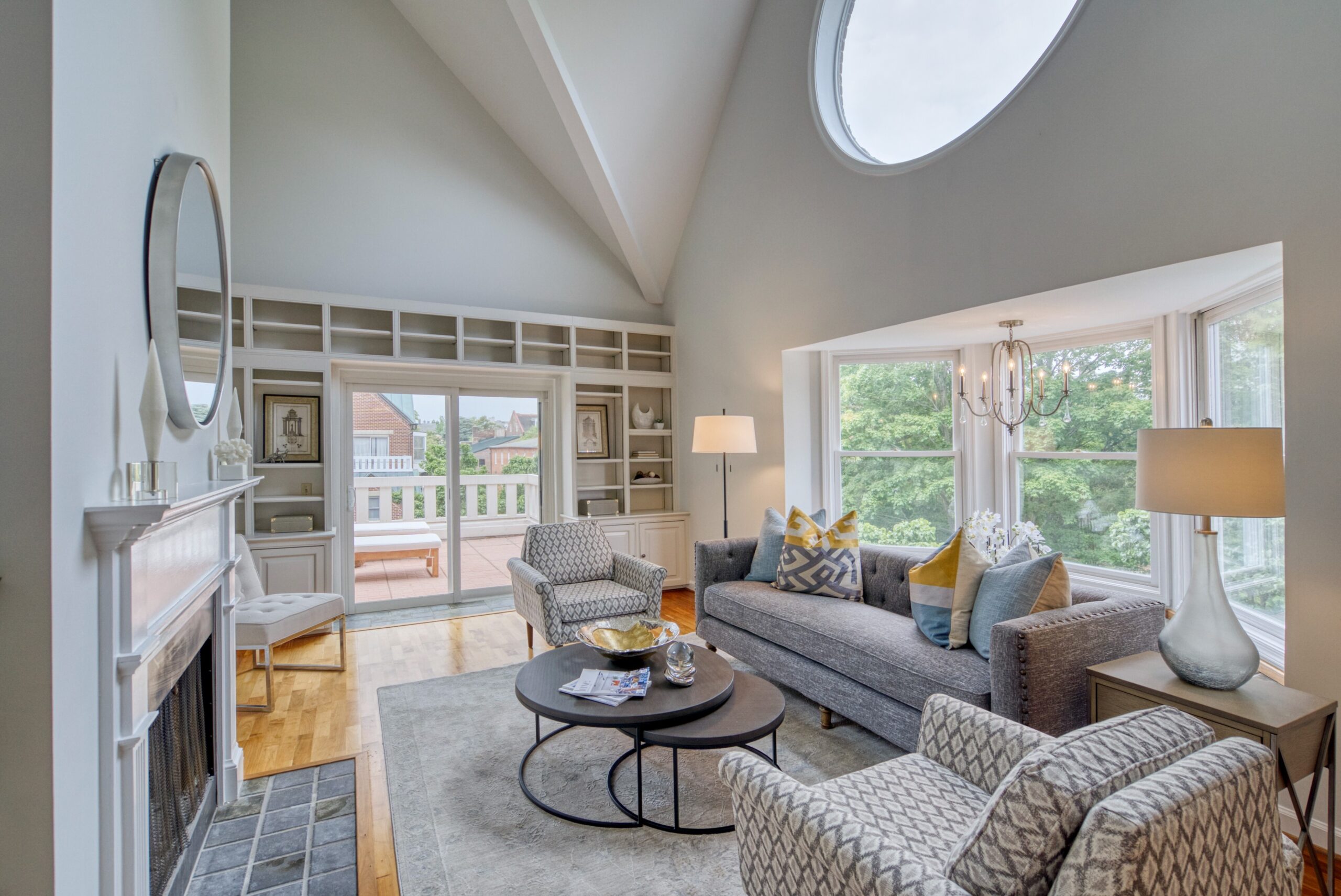Professional interior photo of 125 N Lee St #401, Alexandria, VA - showing the living room with vaulted ceiling, round window over large window nook, built-in bookshelves at the far wall before the balcony