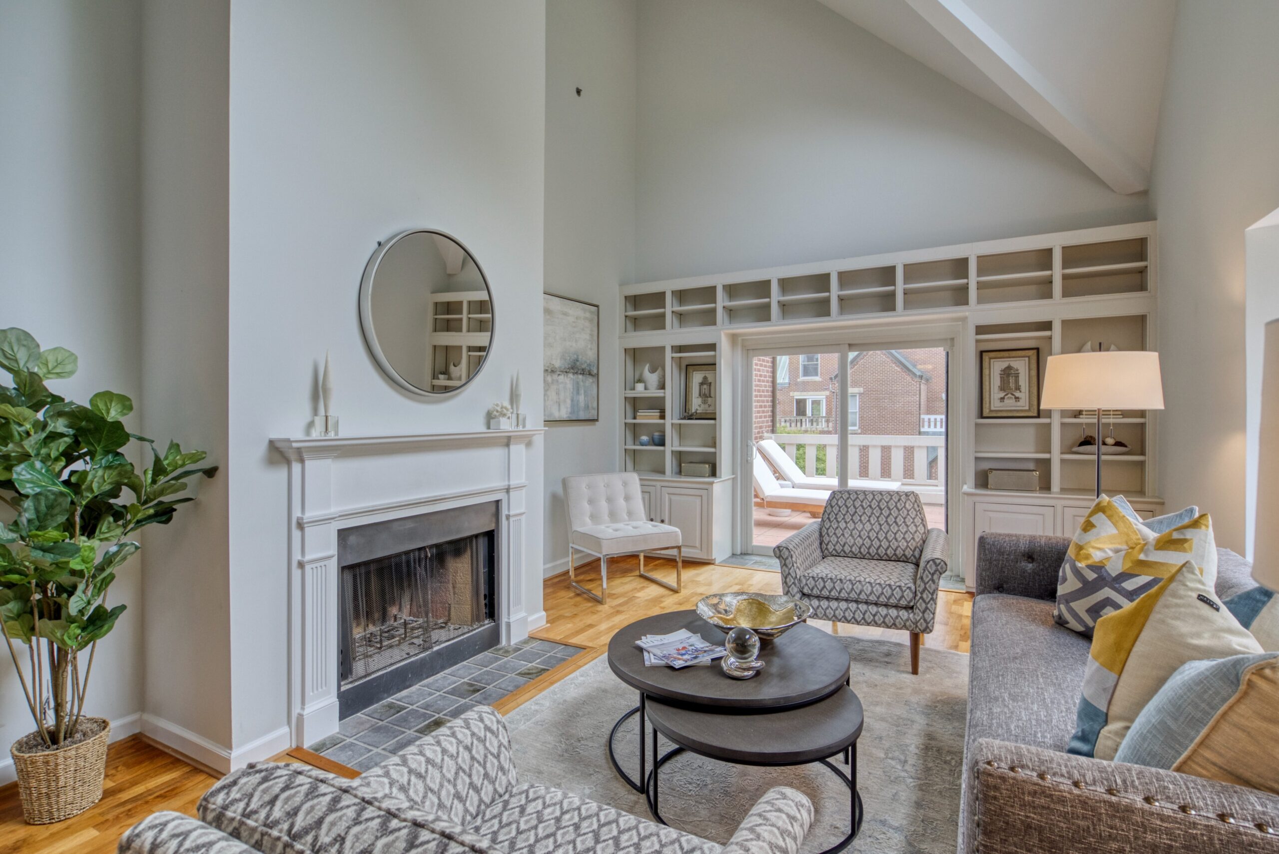 Professional interior photo of 125 N Lee St #401, Alexandria, VA - showing the living room with vaulted ceiling, fireplace, built-in bookshelves at the far wall before the balcony and hardwood floors