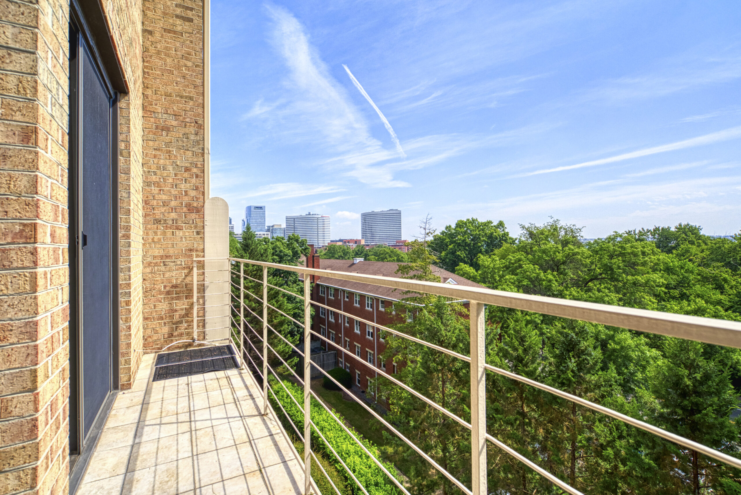 Professional exterior photo of 1215 N Nash St #1, Arlington - showing the rear view off of the living room balcony with trees in the foreground and the Washington DC Skyline in the background