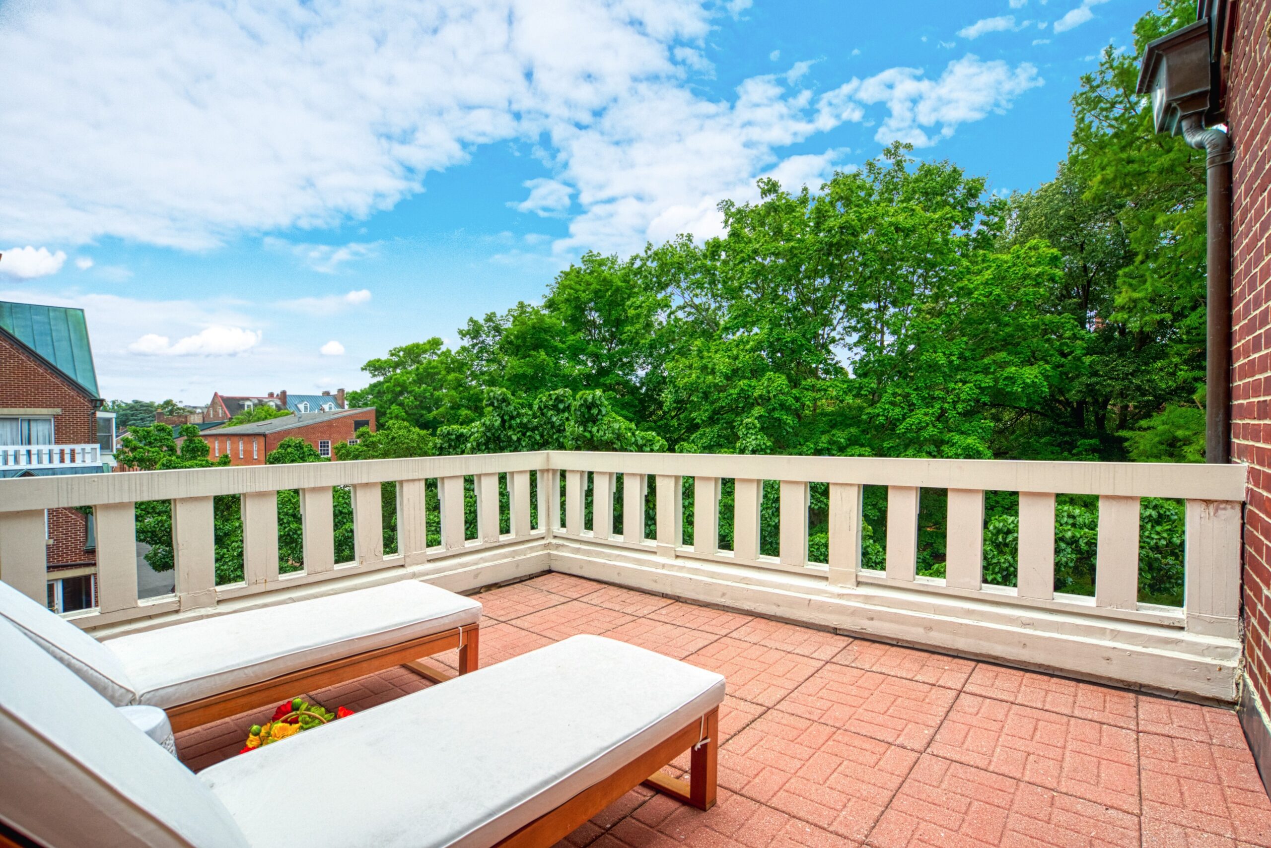 Professional exterior photo of 125 N Lee St, Alexandria, VA - showing the balcony of unit #401 with brick patio and 2 wood and cream lounge chairs