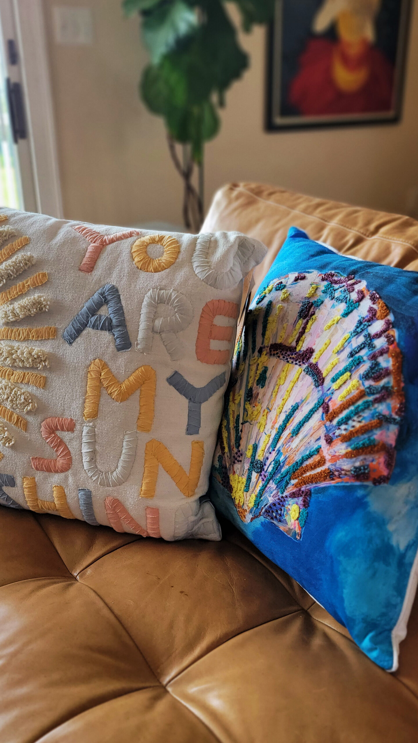 sample prop for Sky Blue Media's Summer Vibes promo service: Showing 2 decorative throw pillows on a camel leather couch. Pillows say "You are my sunshine" and the other had a multicolor shell embroidery