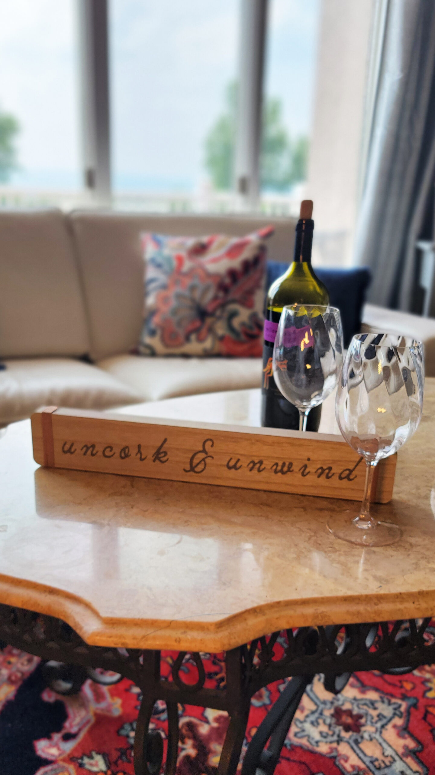 sample prop for Sky Blue Media's Summer Vibes promo service: Showing "uncork & unwind" wooden table decoration with 2 glasses and a wine bottle in the background
