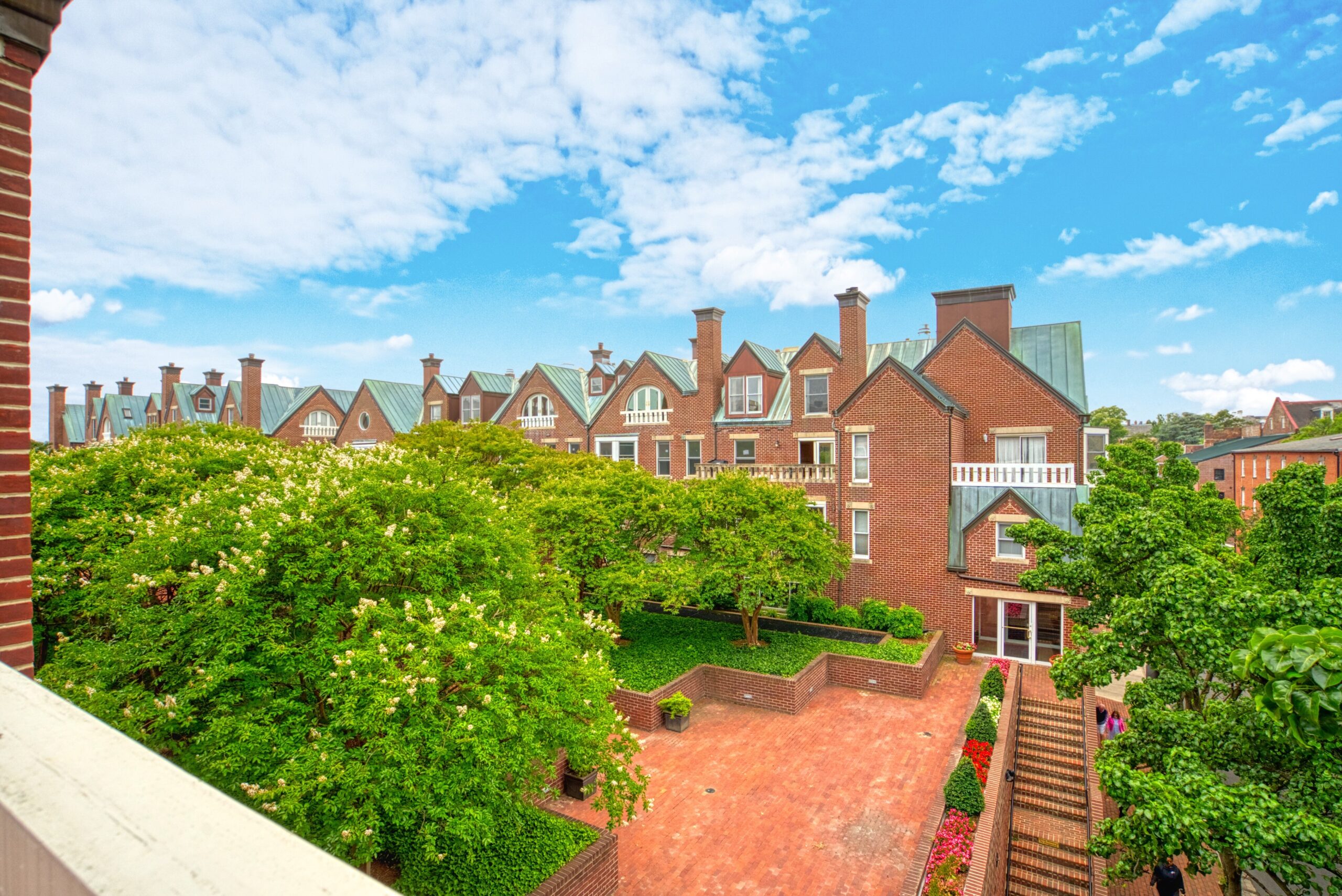 Professional exterior photo of 125 N Lee St, Alexandria, VA - showing the view from the balcony of unit #401 which is a brick courtyard with stairs and mature trees