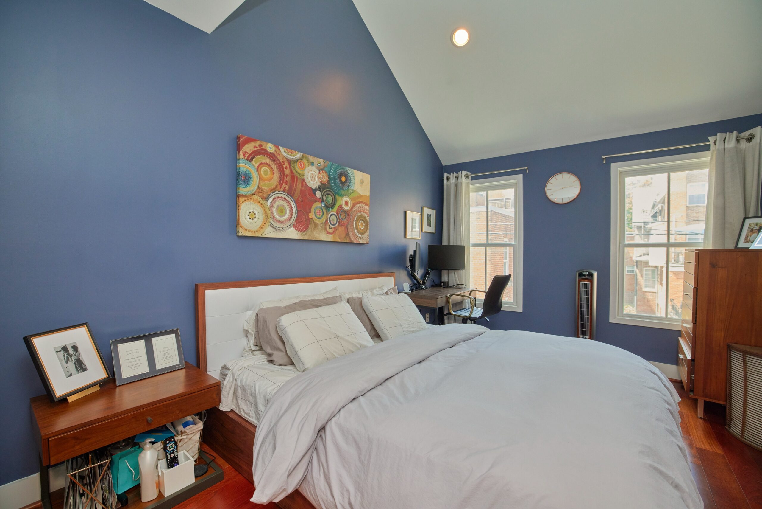 Professional interior photo of 1459 Harvard St NW #6 - showing the primary bedroom on the main floor with vaulted irregular ceiling and hardwood floors and large bed.
