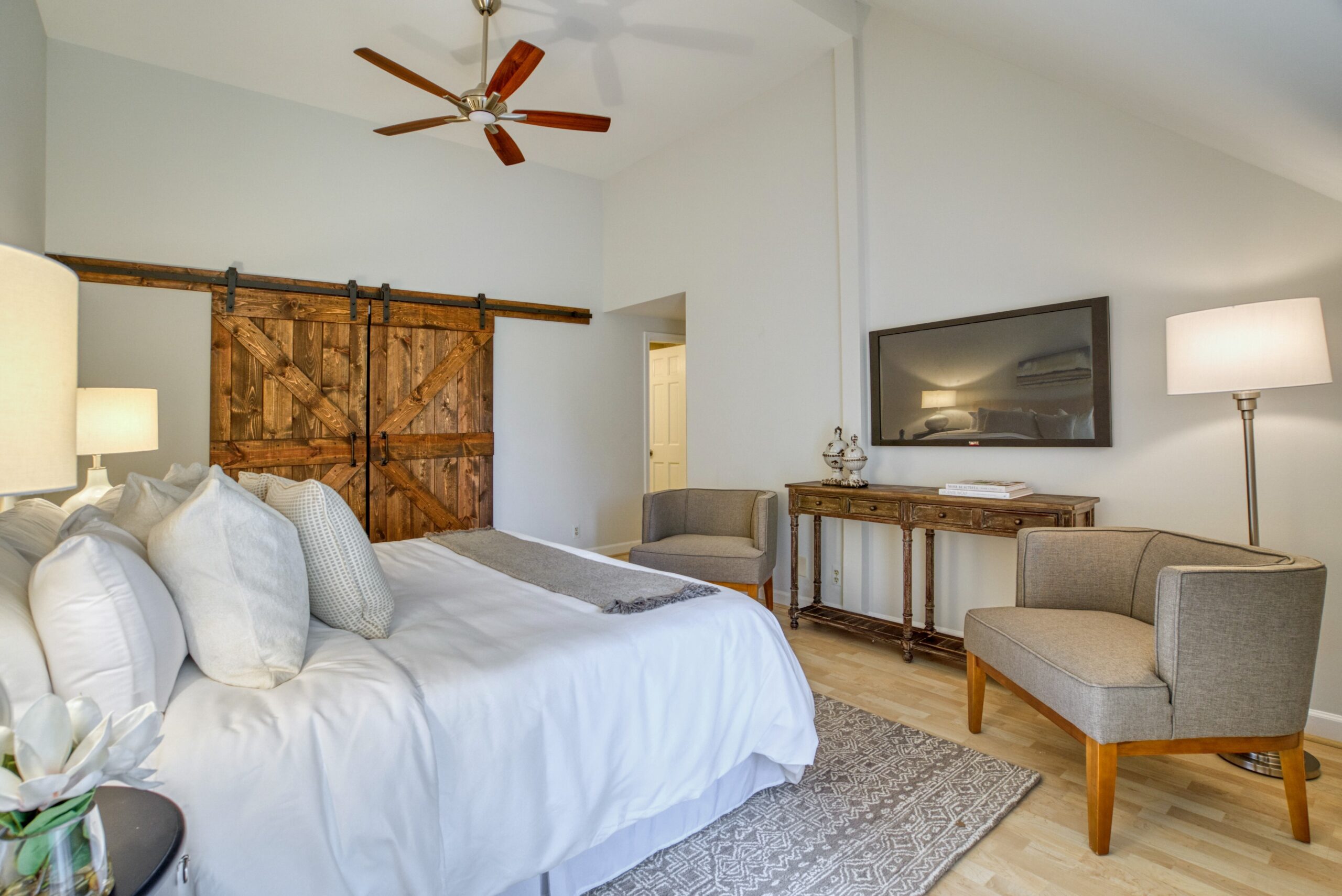 Professional interior photo of 125 N Lee St #401, Alexandria, VA - showing the primary bedroom with barn doors covering the closet, vaulted ceilings and hardwood floors
