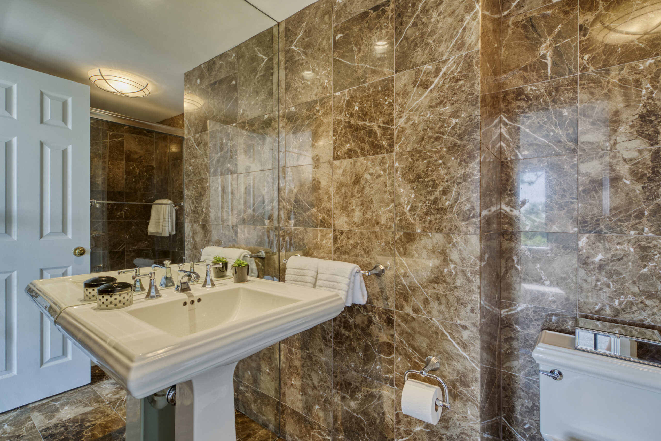 Professional interior photo of 1215 N Nash St #1, Arlington - showing the primary full bathroom sink area with brown marble effect tile on surrounding walls and shower reflecting in the mirror