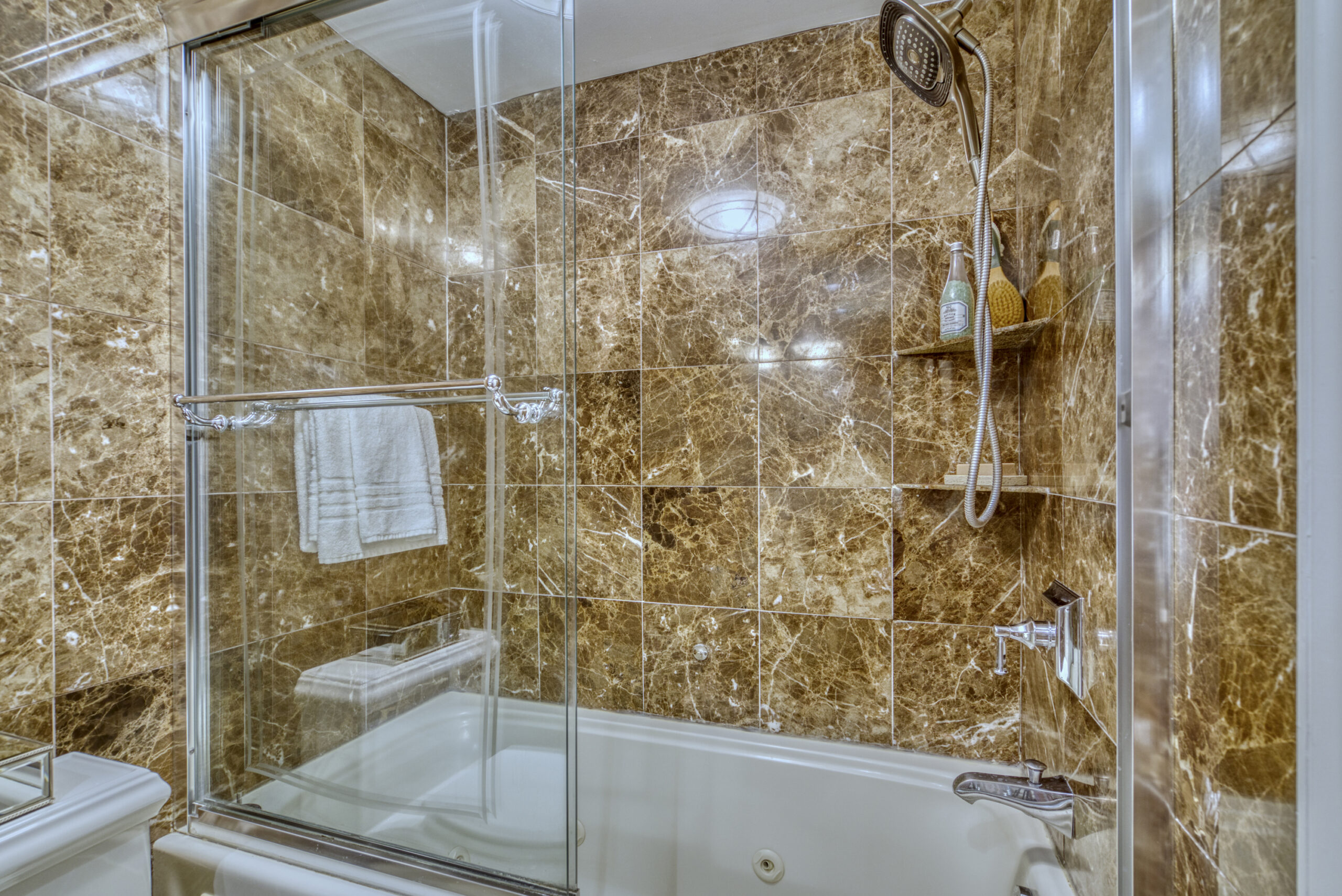 Professional interior photo of 1215 N Nash St #1, Arlington - showing the primary full bathroom shower/tub with brown marble effect tile on surrounding walls and glass sliding doors