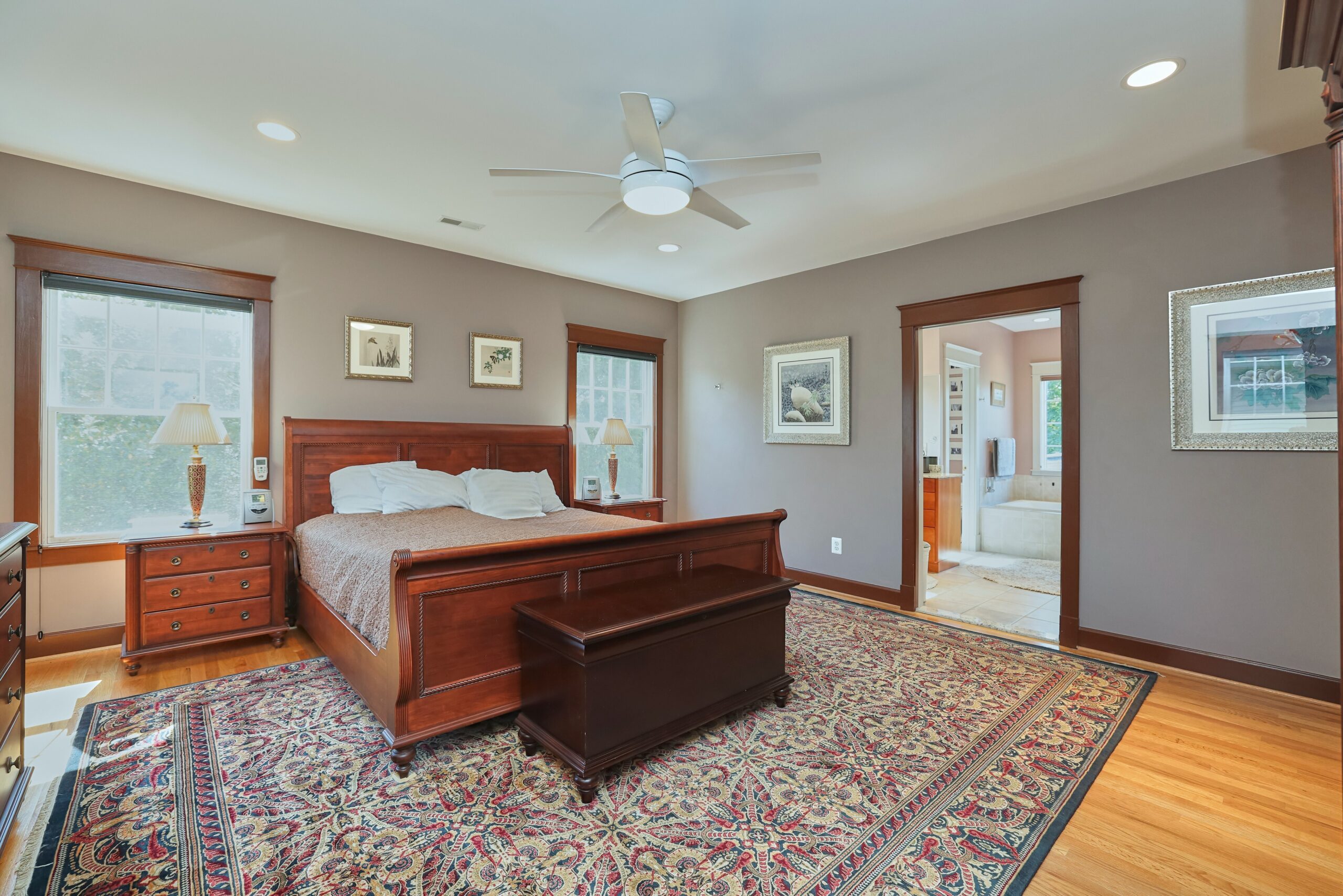 Professional interior photo of 819 N Fillmore St - Showing the primary bedroom with grey walls, ceiling fan, large windows, and view into bathroom