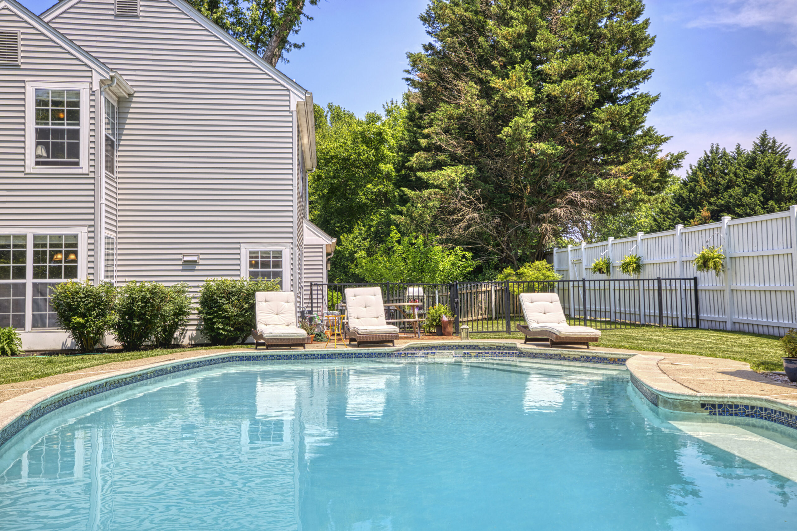 Professional exterior photo of 12309 Stalwart Court - showing the rear of the single family home with grey vinyl siding and the in-ground pool with black metal fence separating the patio area from the brick patio