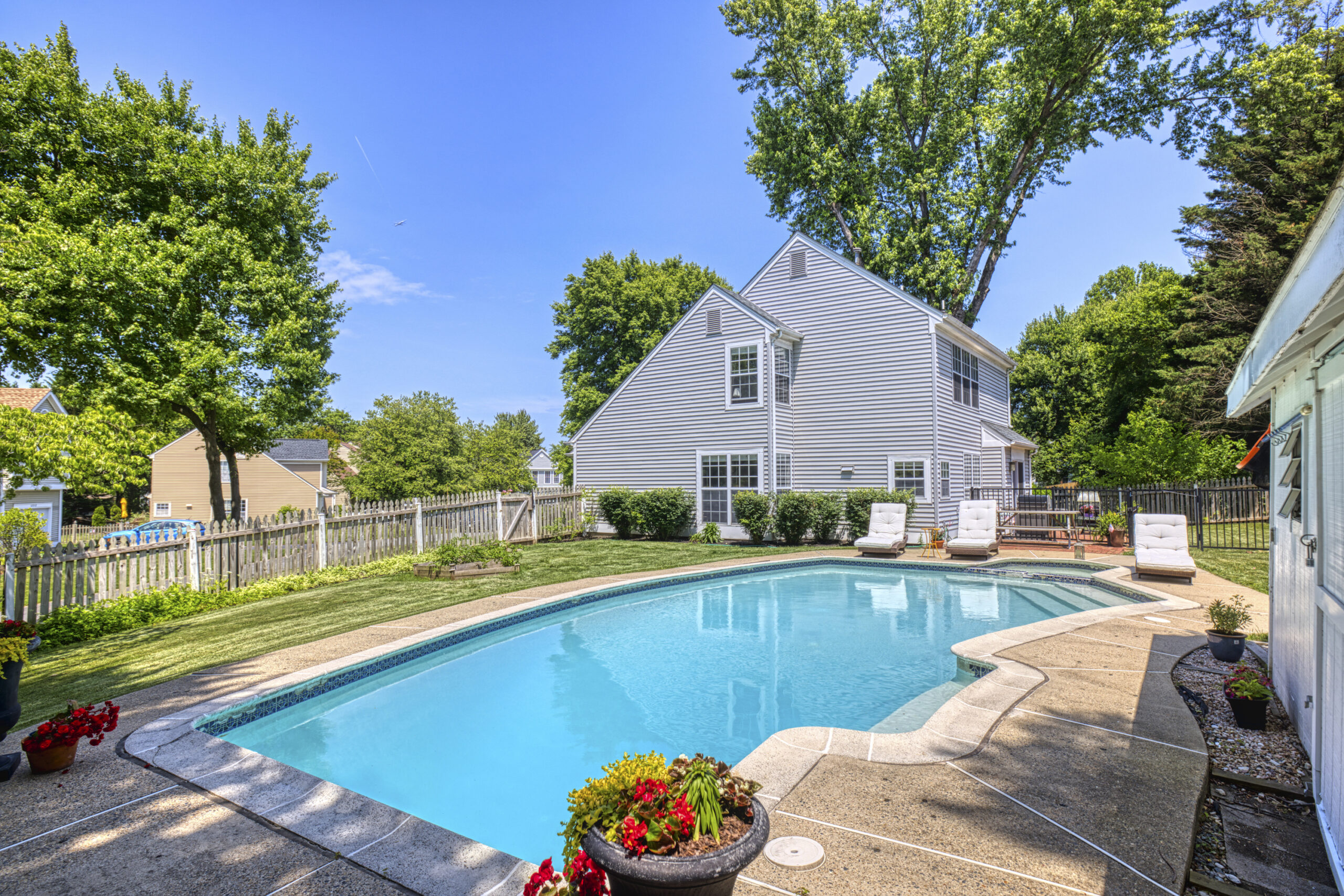 Professional exterior photo of 12309 Stalwart Court - showing the rear of the single family home with grey vinyl siding and the in-ground pool with black metal fence separating the patio area from the brick patio