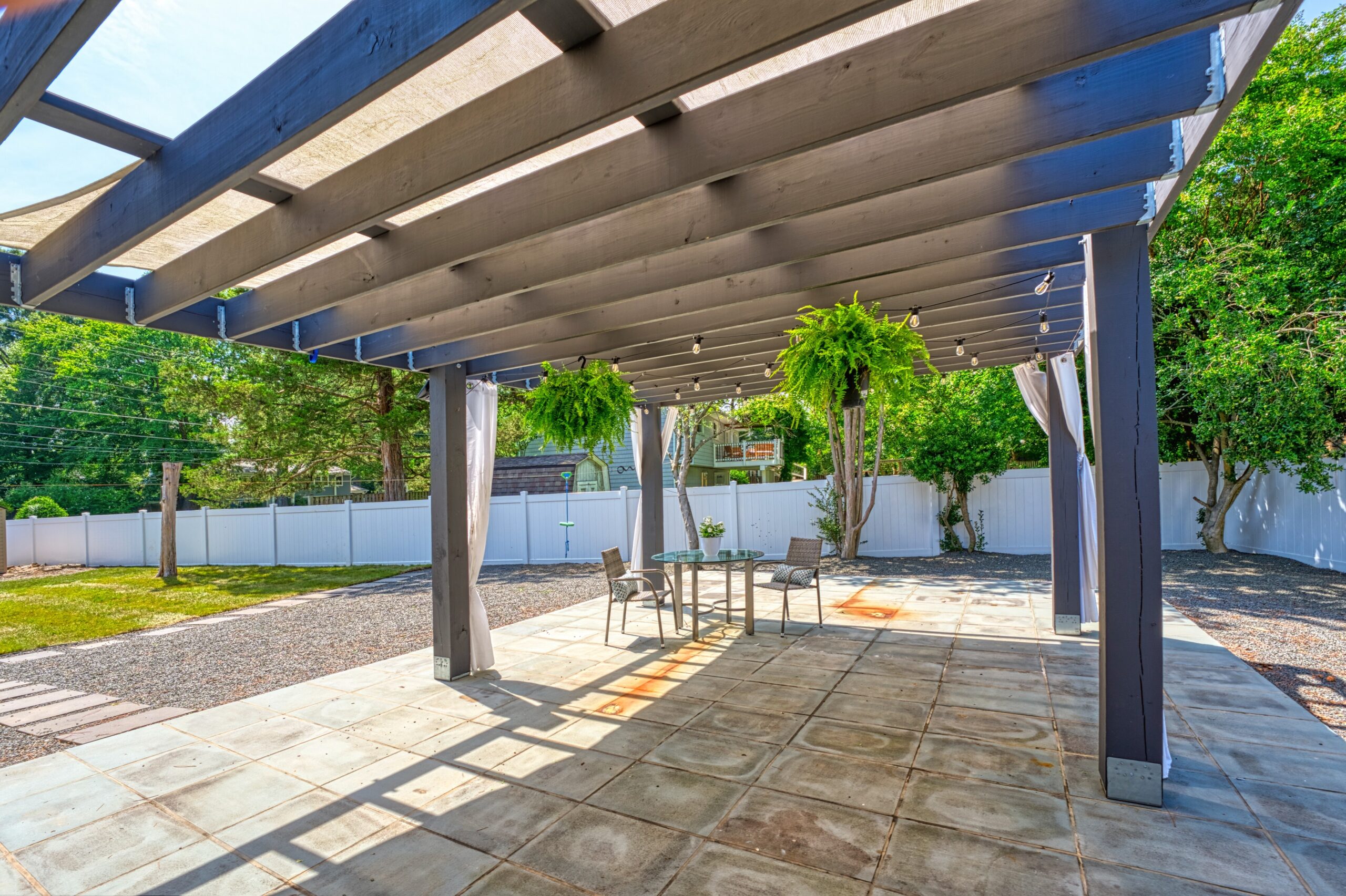 Professional exterior photo of 8320 Fort Hunt Rd, Alexandria - showing the view looking out from the back of the home through a large pergola on an even larger patio with lush landscaping in the background
