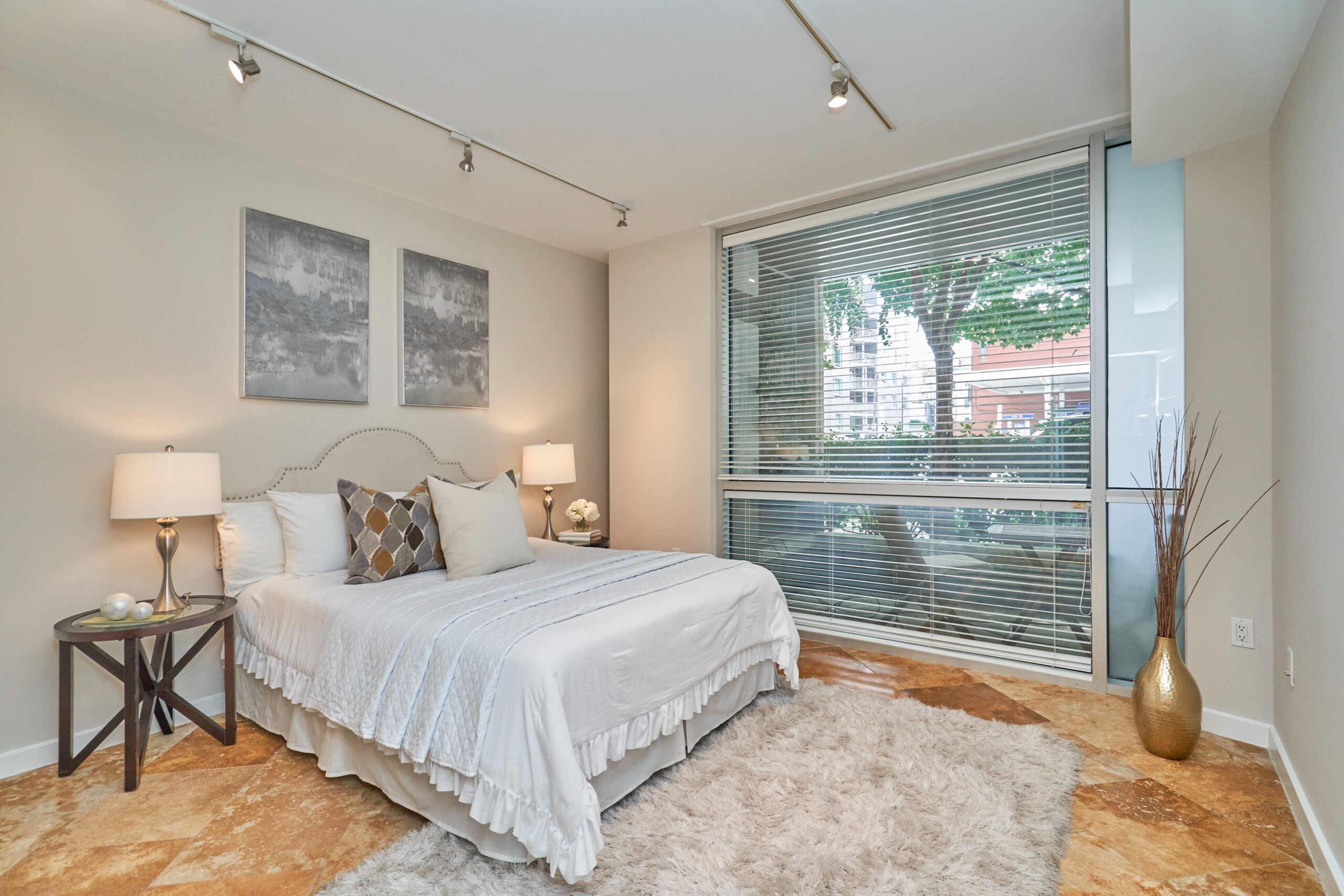 Professional interior photo of 1300 13th St NW #102, Washington DC - showing the primary bedroom with marble floors, floor-to-ceiling windows looking out over the patio