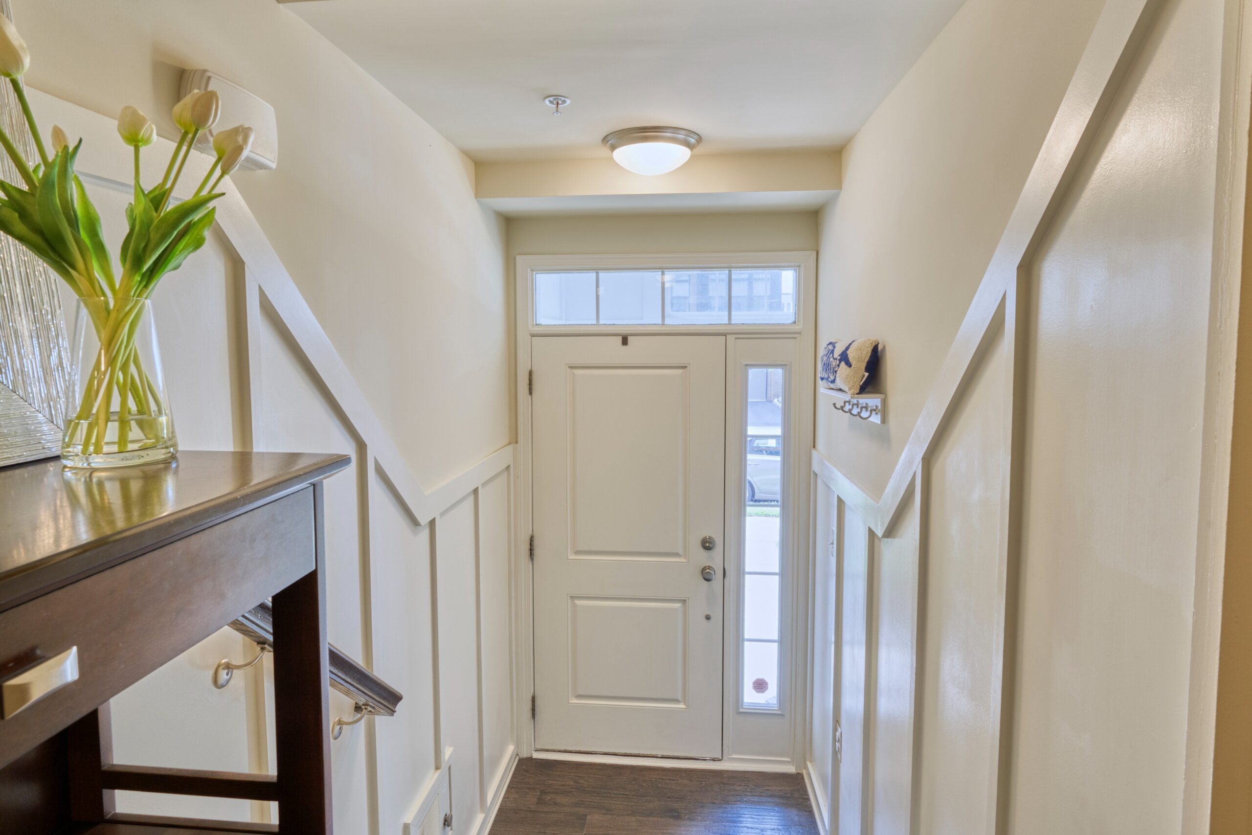 Professional interior photo of 23560 Buckland Farm Ter, Ashburn, VA - Showing the front entry hall with stairs leading up to the main level and white wainscoting against white walls