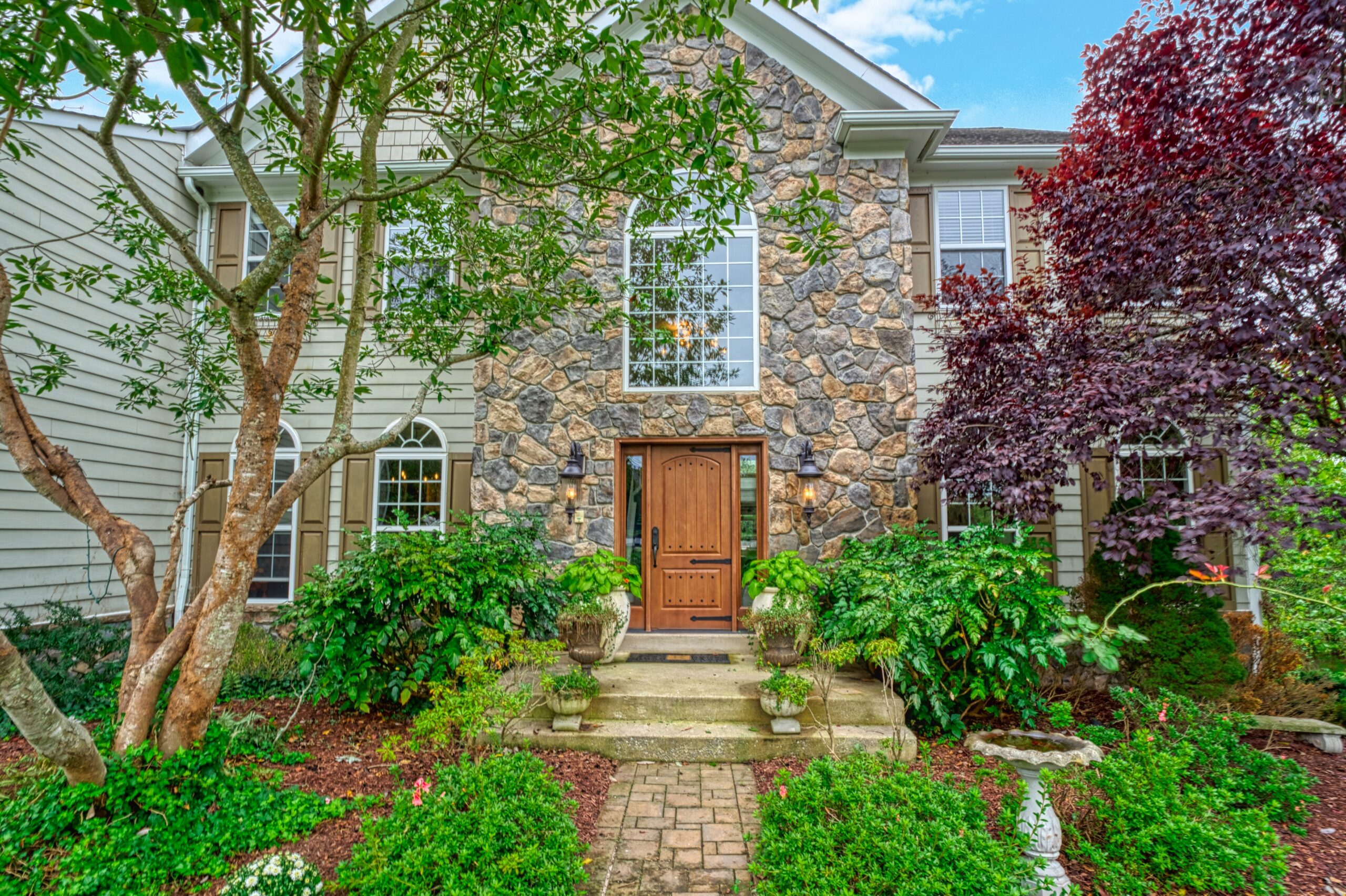 Professional exterior photo of 16961 Heather Knolls Pl - showing the front stone entryway and beige vinyl siding with lush landscaping