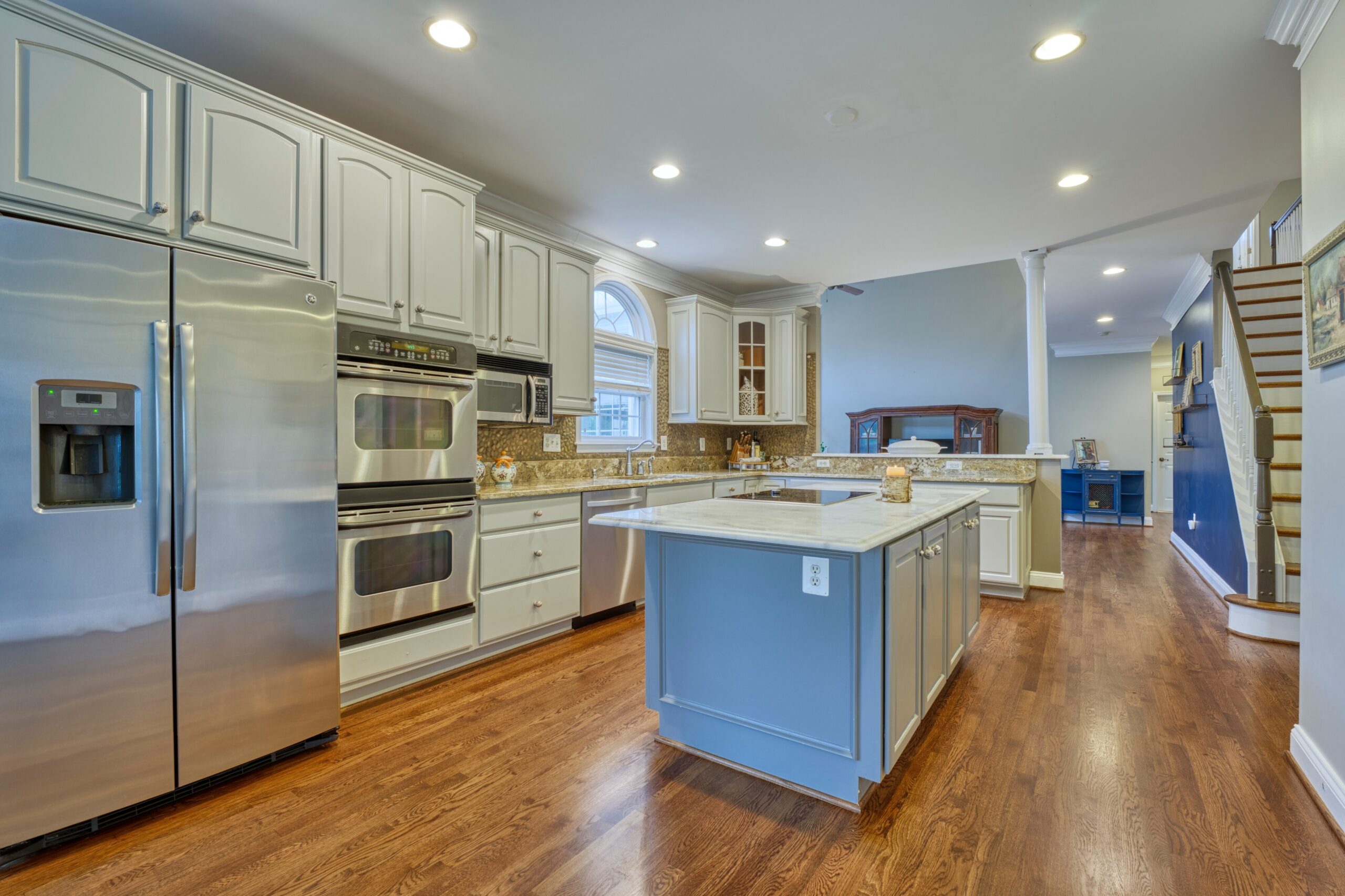 Professional interior photo of 16961 Heather Knolls Pl - showing the kitchen with granite and quartz counters, white cabinets, center island and large double door stainless steel fridge