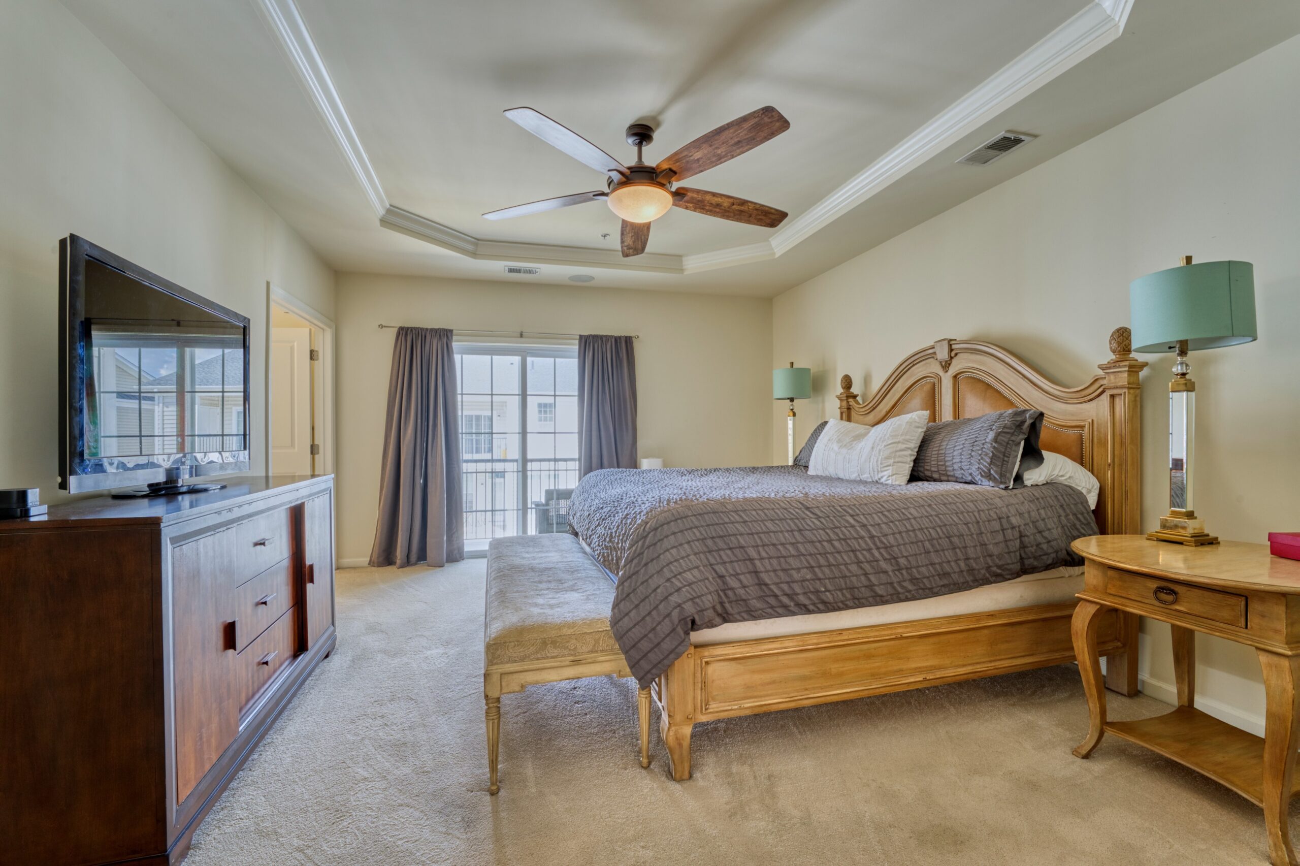 Professional interior photo of 23560 Buckland Farm Ter, Ashburn, VA - Showing the primary bedroom with cream carpeting, tray ceiling, private balcony through sliding doors
