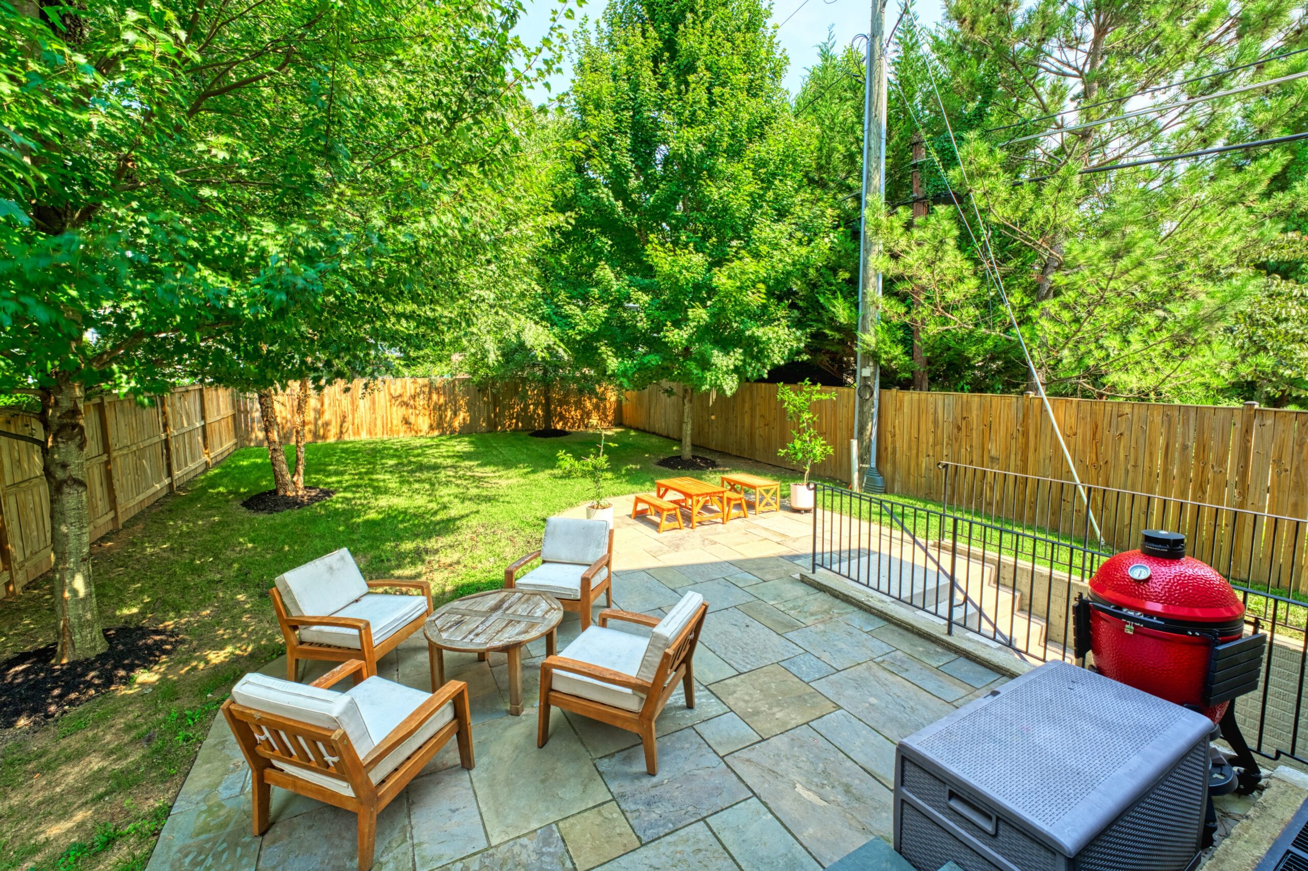 Professional exterior photo of 505 N West St - showing the view of the backyard when standing at the rear sliding door. Stone patio with 2 sets of patio furniture with flat backyard in rear with 4 mature trees, fully fenced