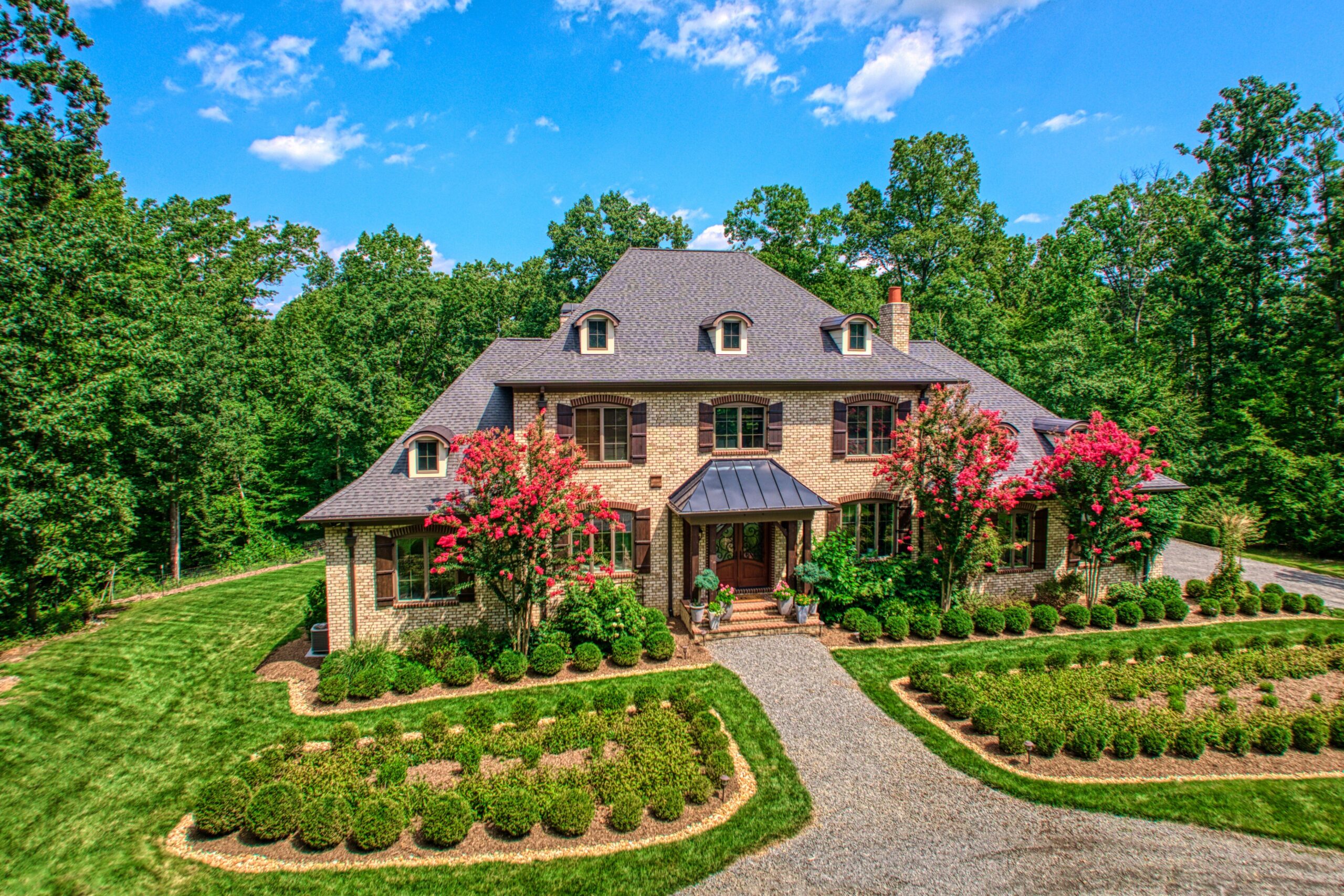 Professional exterior photo of 40046 Mount Gilead Rd in Leesburg, Virginia - showing the front of a french country style home with cream stone facade, ornate gardens that line either side of a gravel path to the front entrance