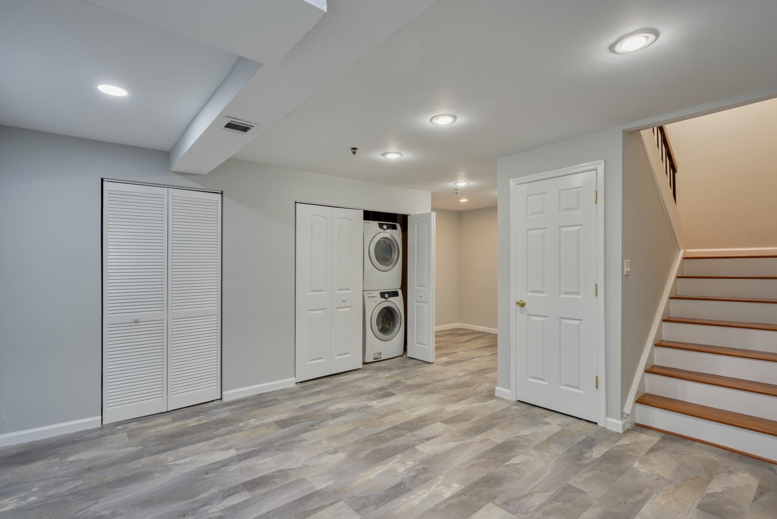 Professional interior photo of 6302 Arwen Court, Fort Washington, MD - showing the basement with new grey LVP flooring, storage closets and laundry closet and stairs leading to the main level