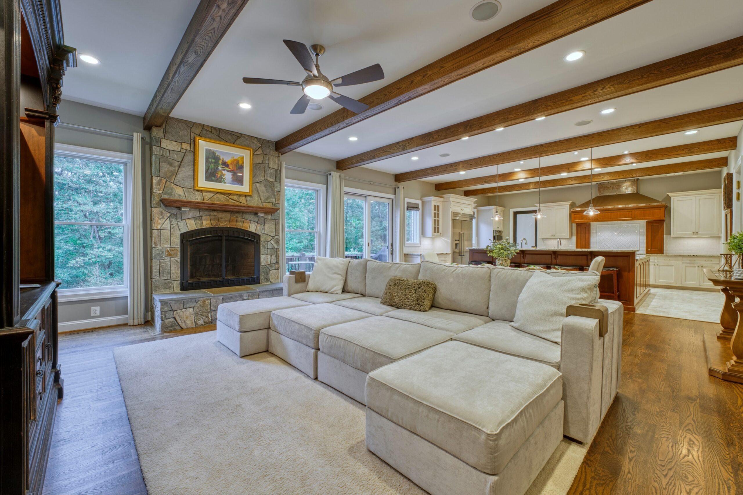Professional interior photo of 40046 Mount Gilead Rd in Leesburg, Virginia - showing the living room open to the kitchen with large exposed beams in the otherwise white ceiling. There is a stone fireplace against the back wall