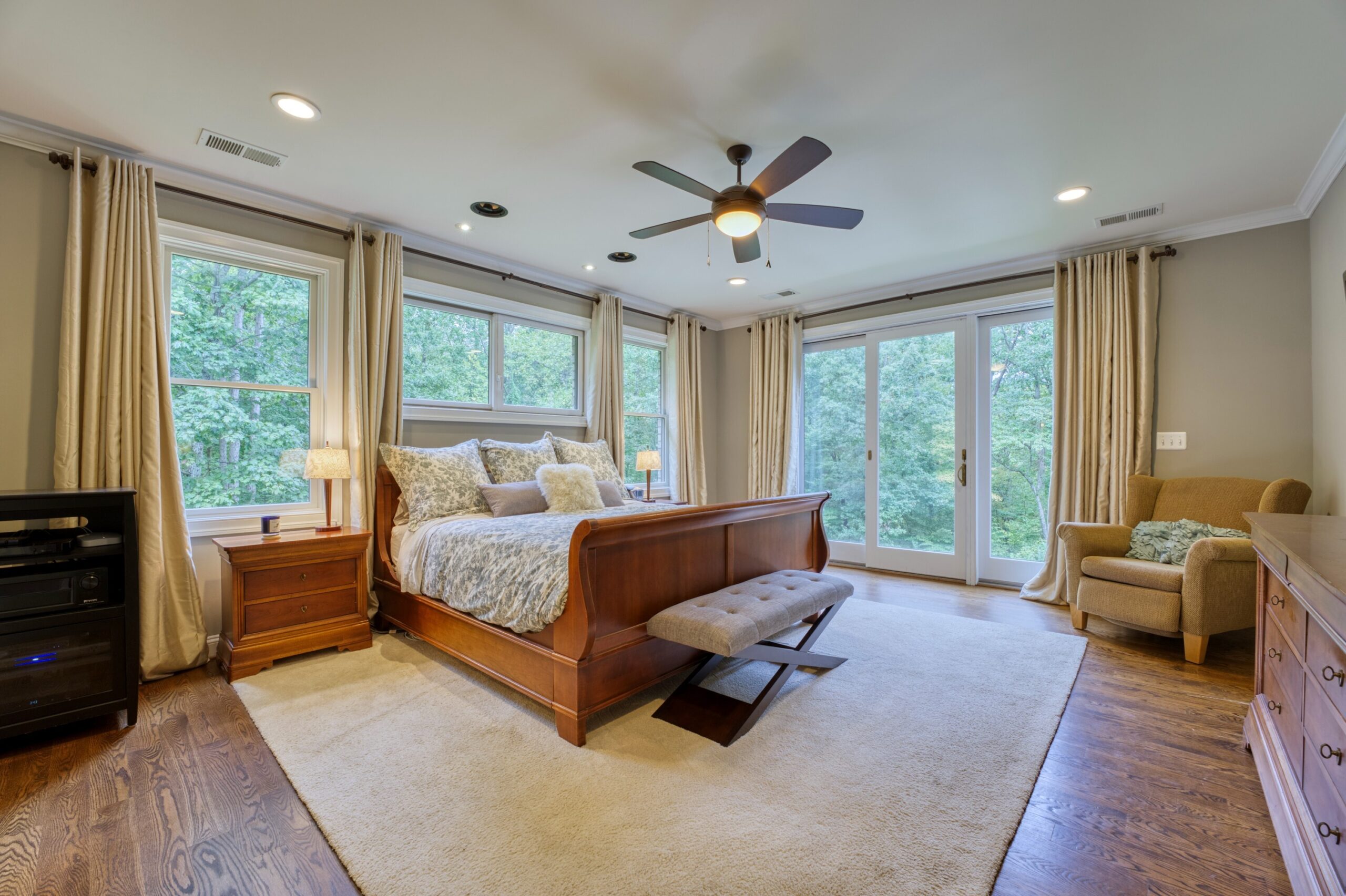 Professional interior photo of 40046 Mount Gilead Rd in Leesburg, Virginia - showing the main floor primary bedroom with huge windows on two walls, hardwood floors, and views of the woods