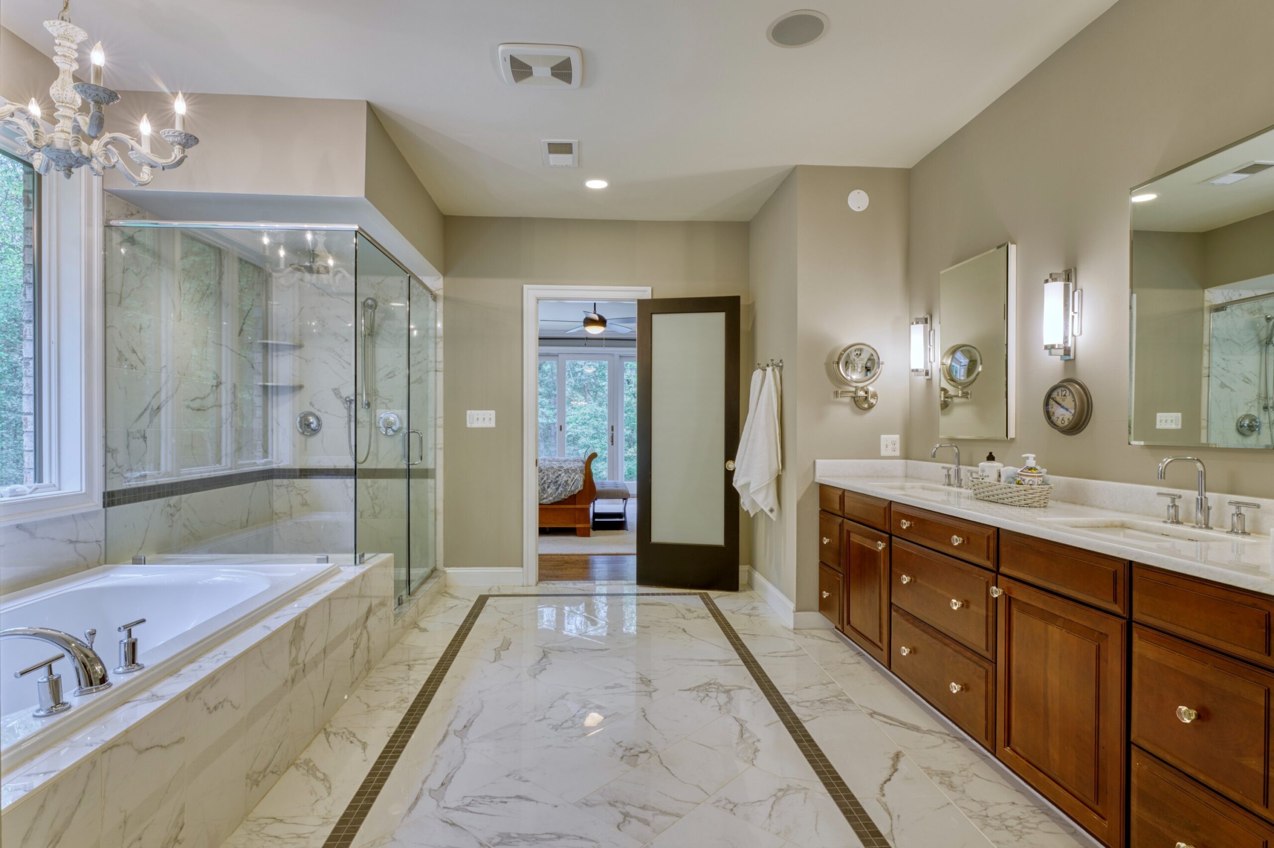 Professional interior photo of 40046 Mount Gilead Rd in Leesburg, Virginia - showing the primary bathroom for the main floor bedroom with marble floor, looking back towards the bedroom with expansive dual vanity on the right and a soaking tub next to a walk in enclosed shower on the left side.