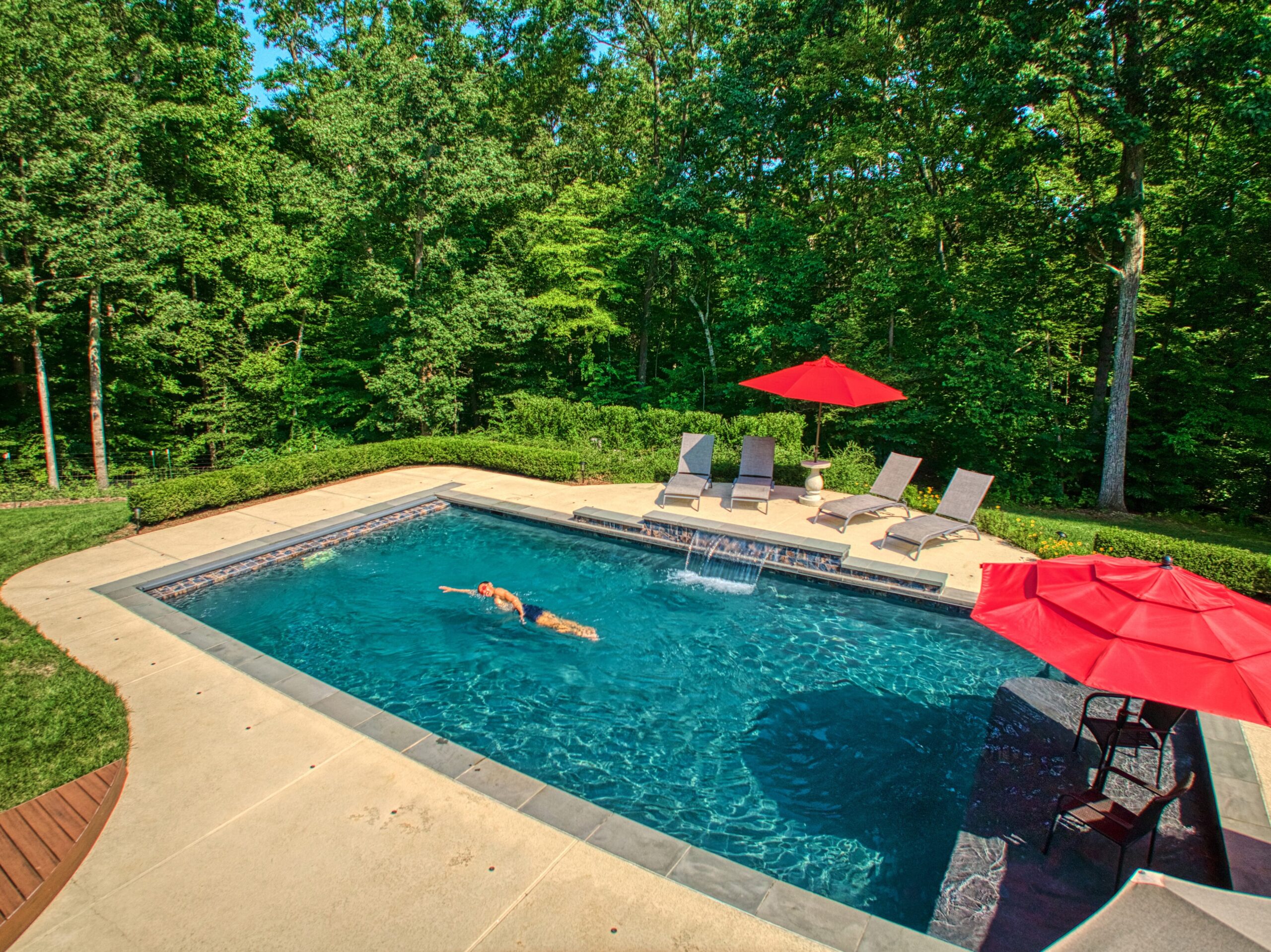 Professional exterior photo of 40046 Mount Gilead Rd in Leesburg, Virginia - showing the in ground pool with waterfall on a sunny day while a man does laps