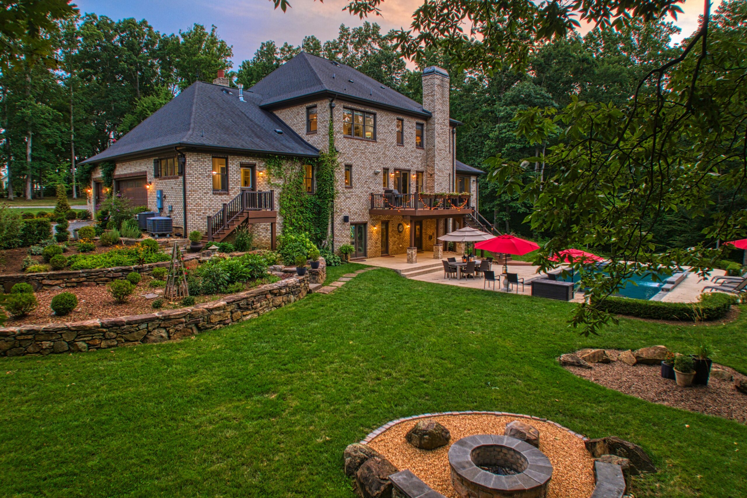 Professional exterior photo of 40046 Mount Gilead Rd in Leesburg, Virginia - showing the rear of the stone home with terraced landscaping, a fire pit, and looking back towards the house there is a deck, terrace and inground pool