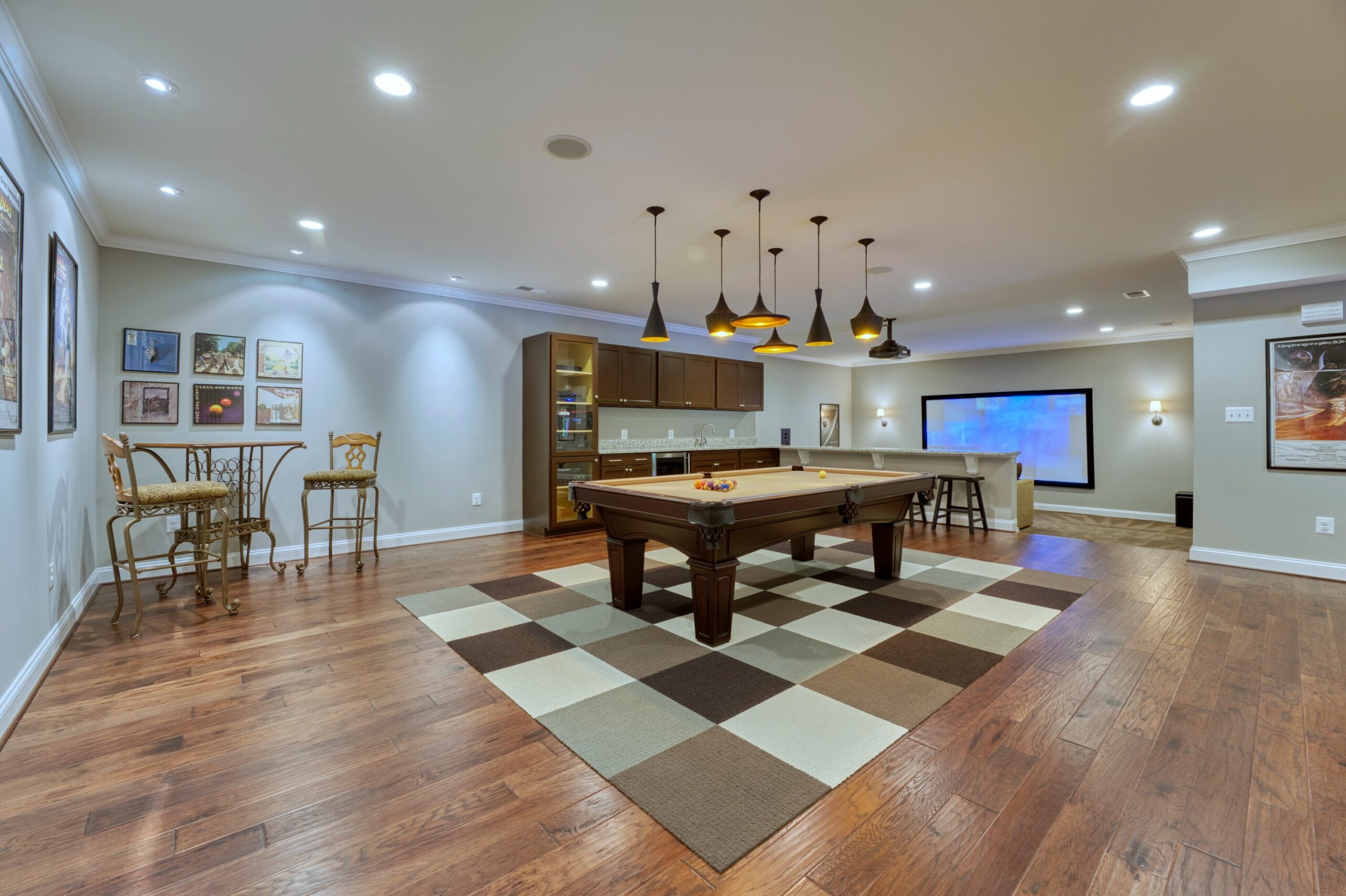 Professional interior photo of 40046 Mount Gilead Rd in Leesburg, Virginia - showing the billiards room with bar table and stools, bar area and media room in the background