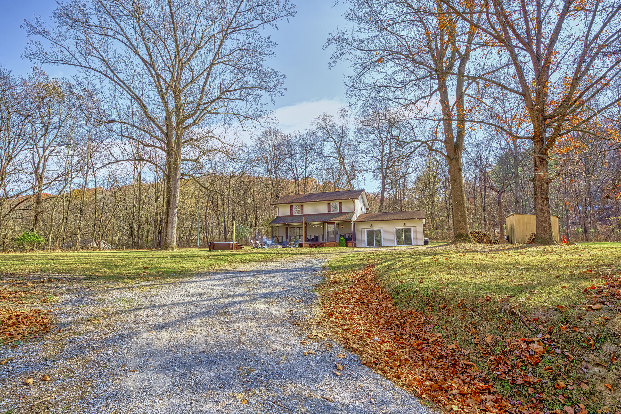 Professional exterior photo of 4809 Grove Hill River Rd - showing the view looking up the driveway to the front of a transitional 2-story home with screened front porch, front stone patio with fire pit and nearby hot tub