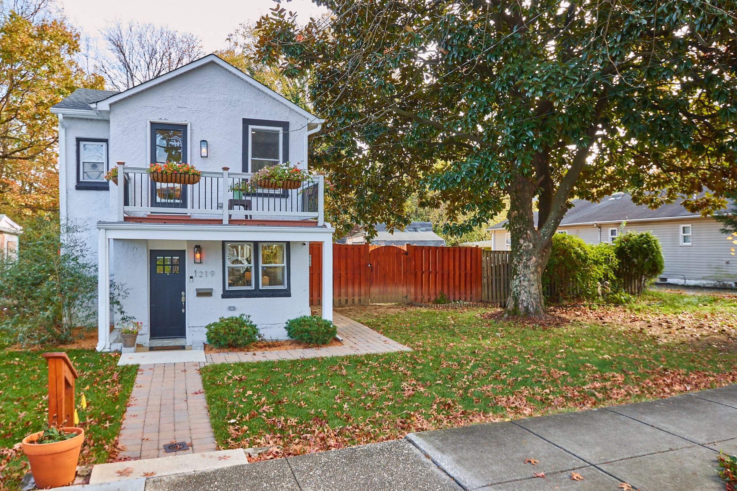 Professional exterior photo of 1219 50th St NE in Washington, DC - showing the front view from an angle at the curb and you see a white detached home with balcony and fully fenced backyard