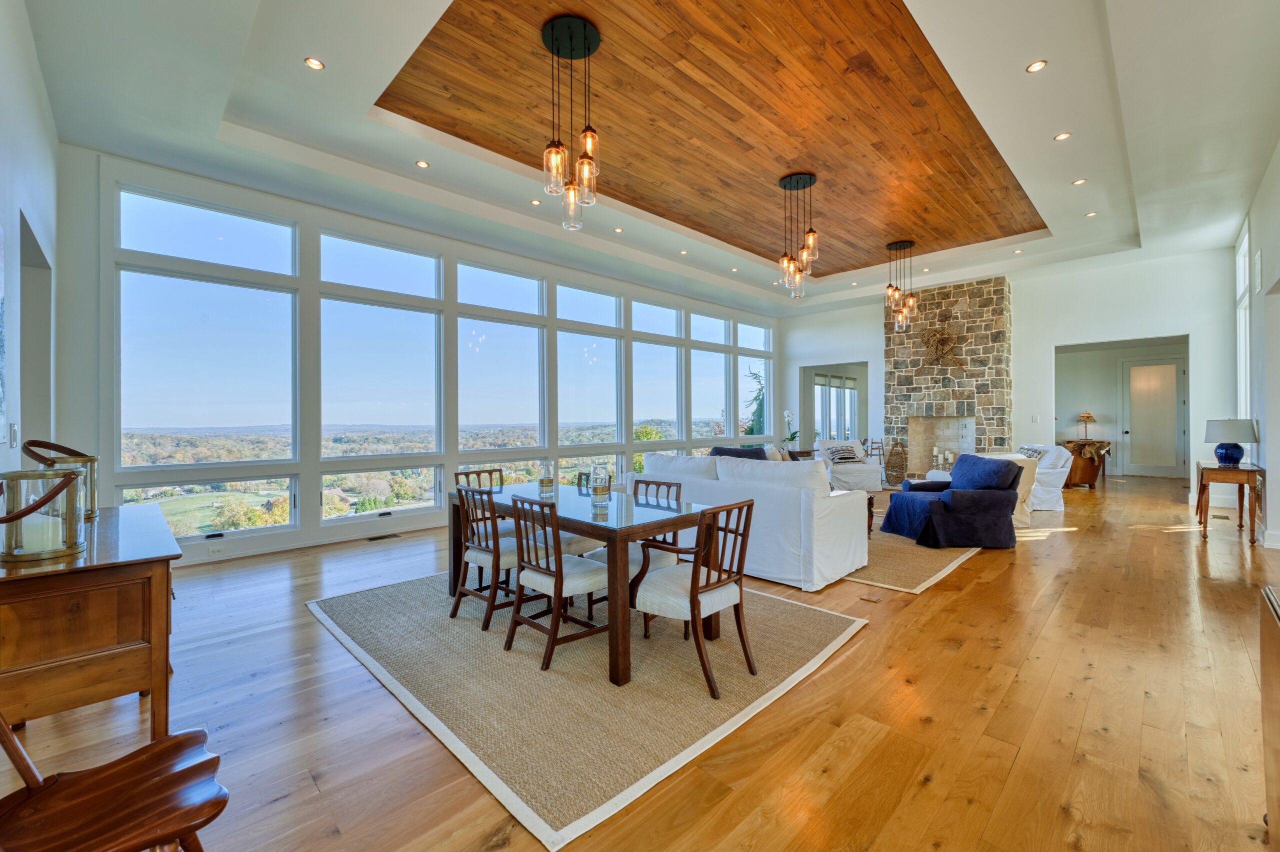 Professional interior photo of 17151 Brookdale Ln in Round Hill, VA - showing the great room with fireplace, recessed hardwood panel on the ceiling, hardwood floors, and large windows on either side to take in the views
