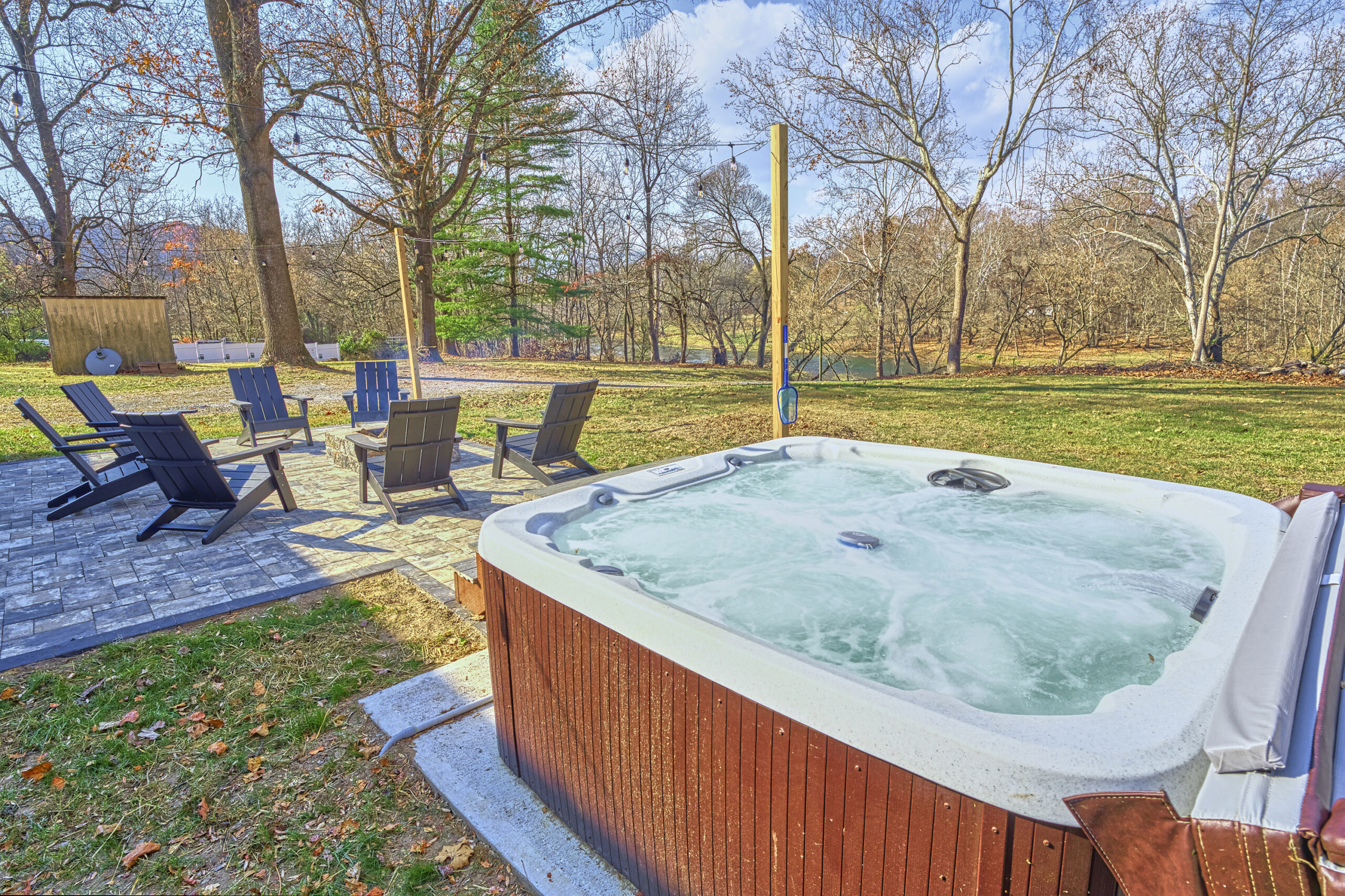 Professional exterior photo of 4809 Grove Hill River Rd - showing the hot tub in the foreground and the stone patio with fire pit in the background in the front yard