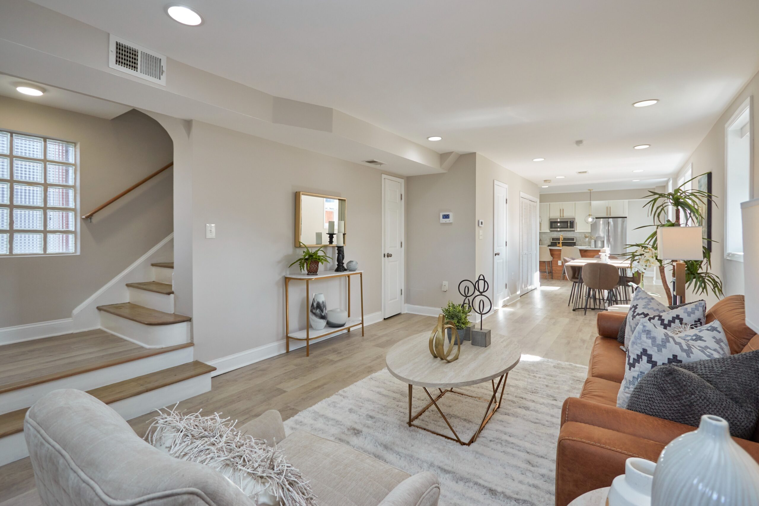 Professional interior photo of 1219 50th St NE in Washington, DC - showing the living room that flows openly back through the dining room to the kitchen and a staircase at the front leading to the second floor