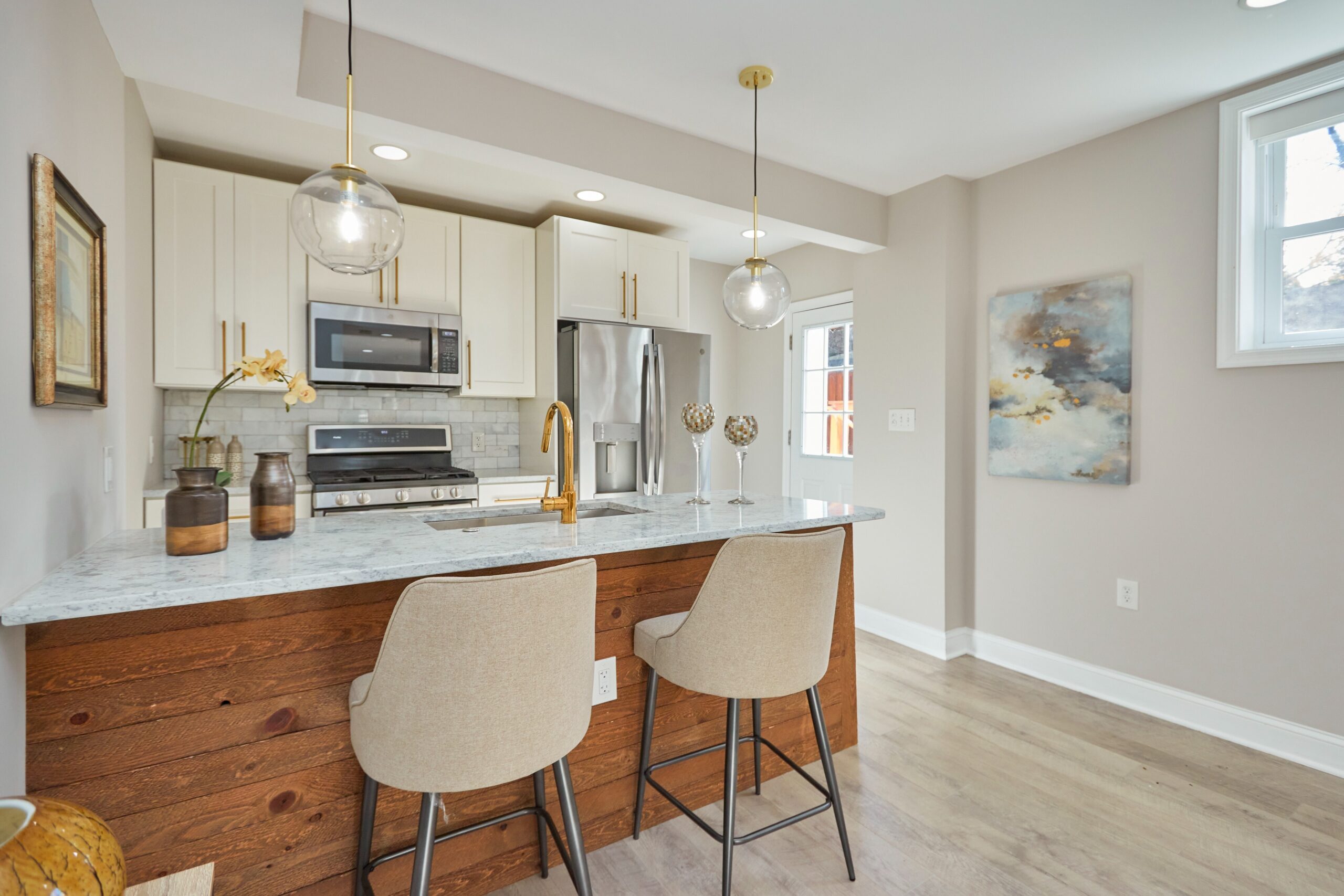 Professional interior photo of 1219 50th St NE in Washington, DC - showing the fully remodeled kitchen with quartz countertop island/peninsula and bar with white cabinets, stainless appliances and brushed cold hardware