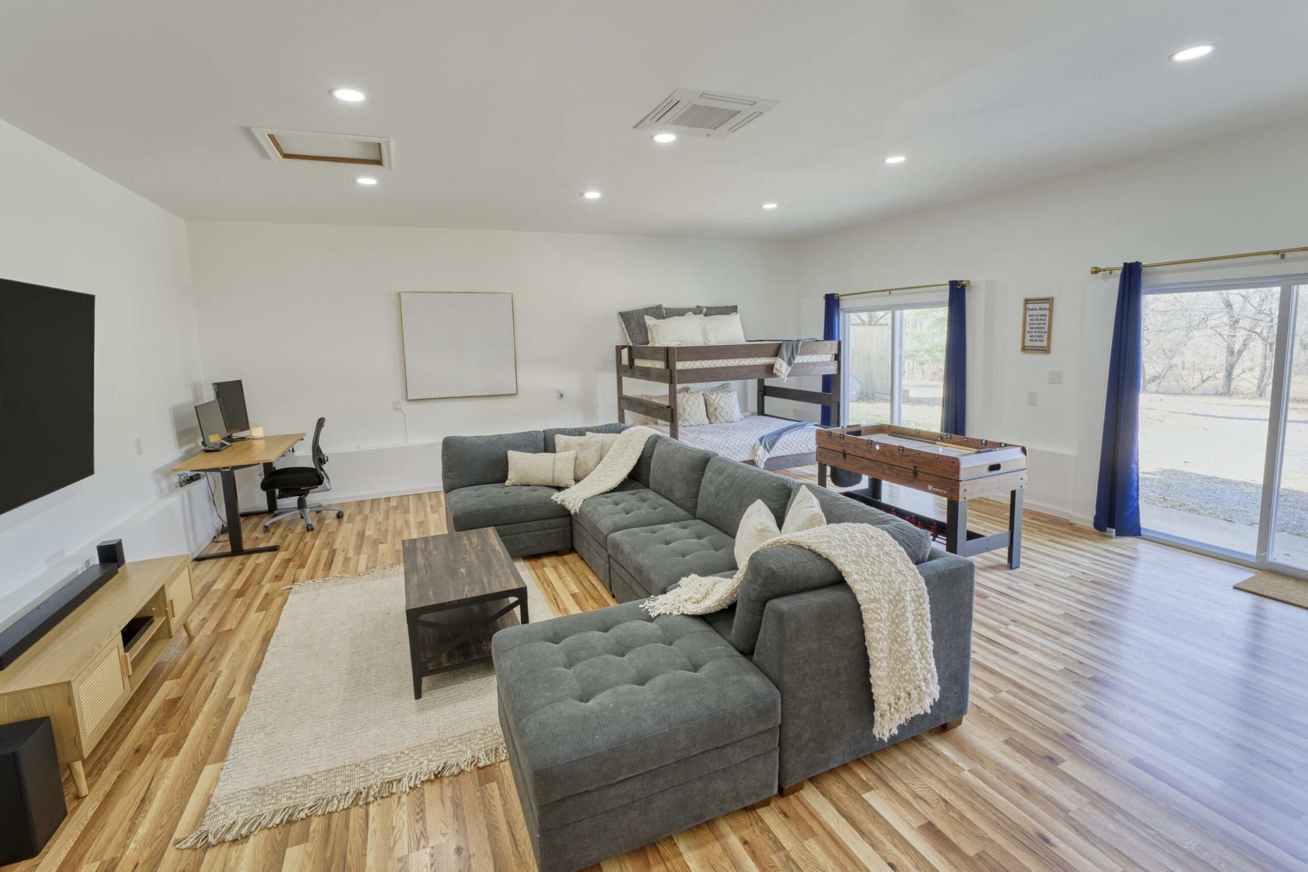 Professional interior photo of 4809 Grove Hill River Rd - showing the basement rec room with mounted big screen tv, sectional couch, bunk beds, foosball table, and 2 sliding doors to the outside of the home