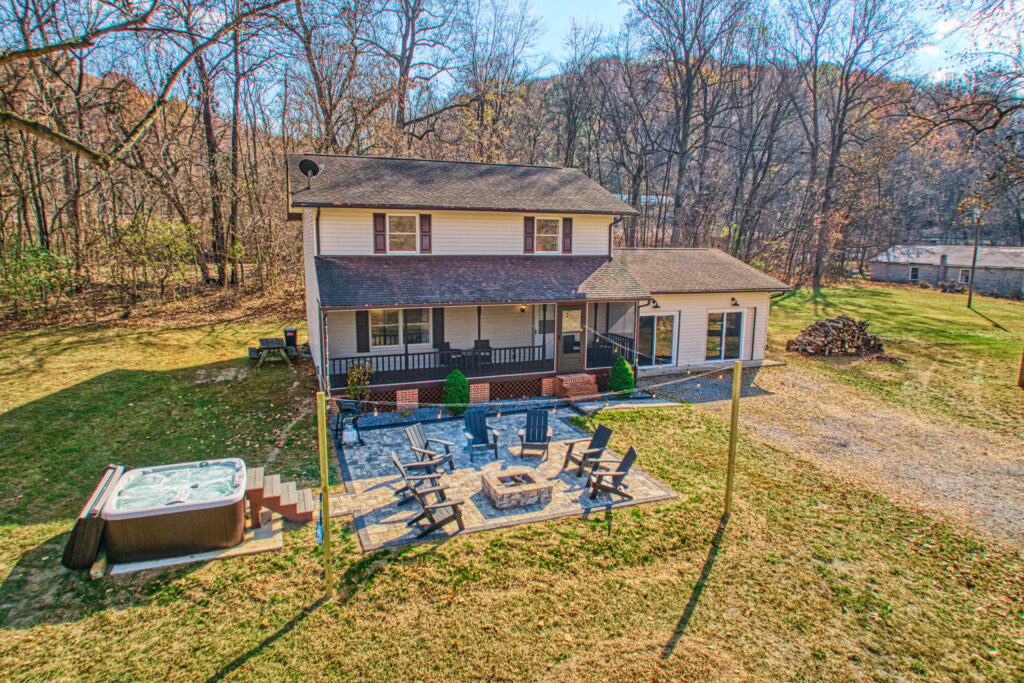 Professional exterior photo of 4809 Grove Hill River Rd - aerial shot of the front of a transitional 2-story home with screened front porch, front stone patio with fire pit and nearby hot tub