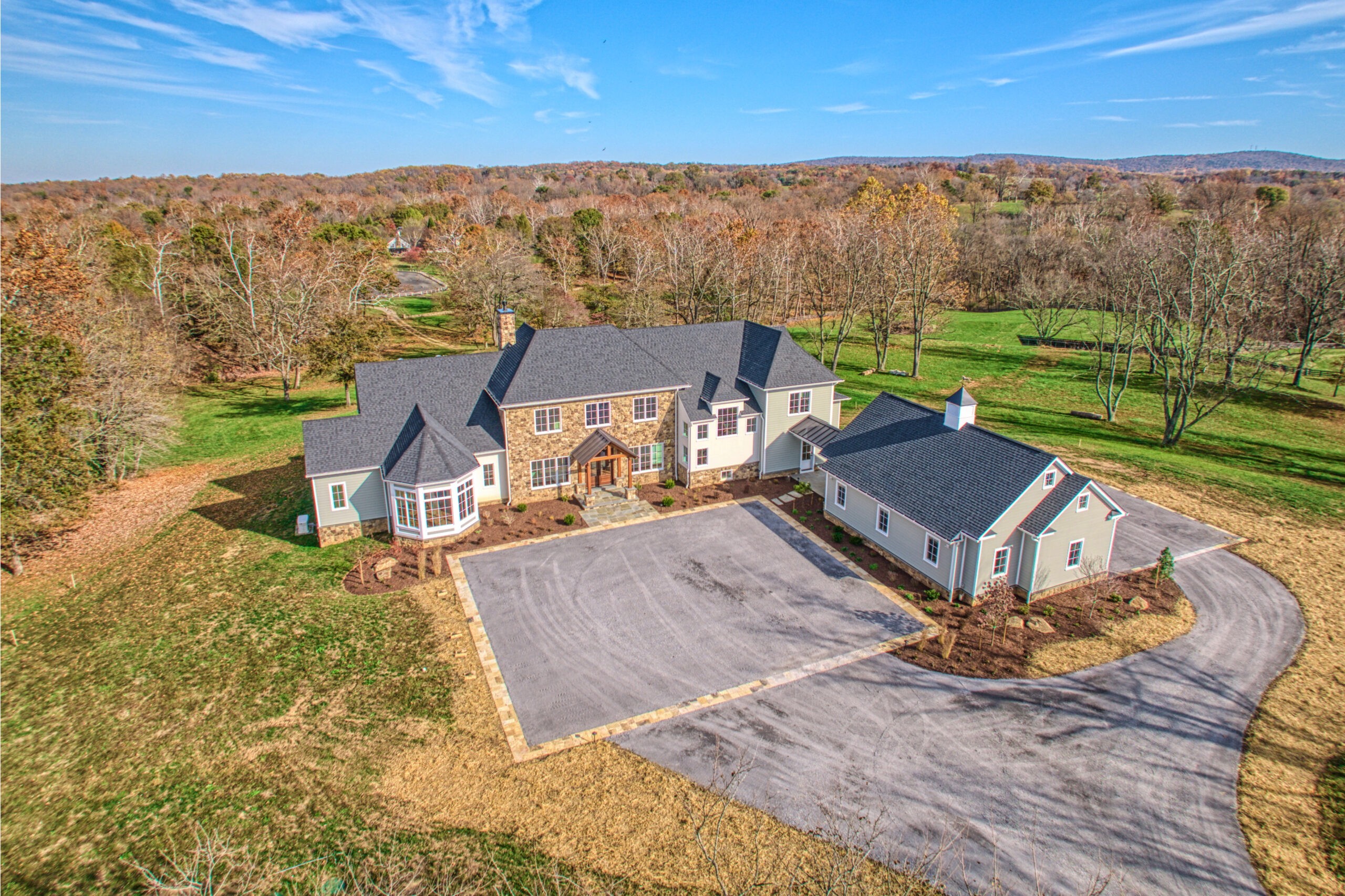 Professional exterior drone photo of custom build home in Middleburg, VA - showing the new single family home with separate 4-car garage, large square parking area in the front and driveway circling around to the rear of the garage