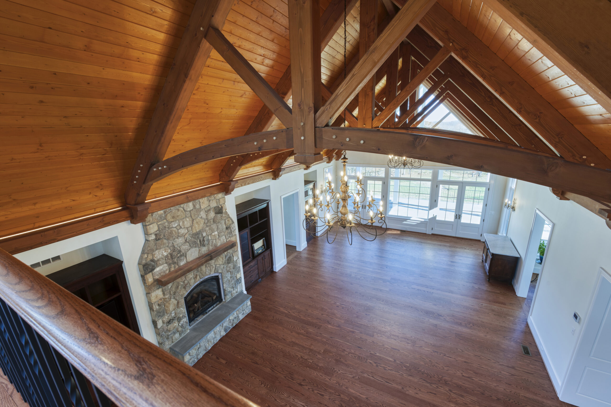 Professional interior photo of custom build new home by Black Oak Construction - showing the great room from the balcony above with hardwood floors, vaulted wooden ceiling with wooden trusses, stone fireplace and built-in cabinets on either side