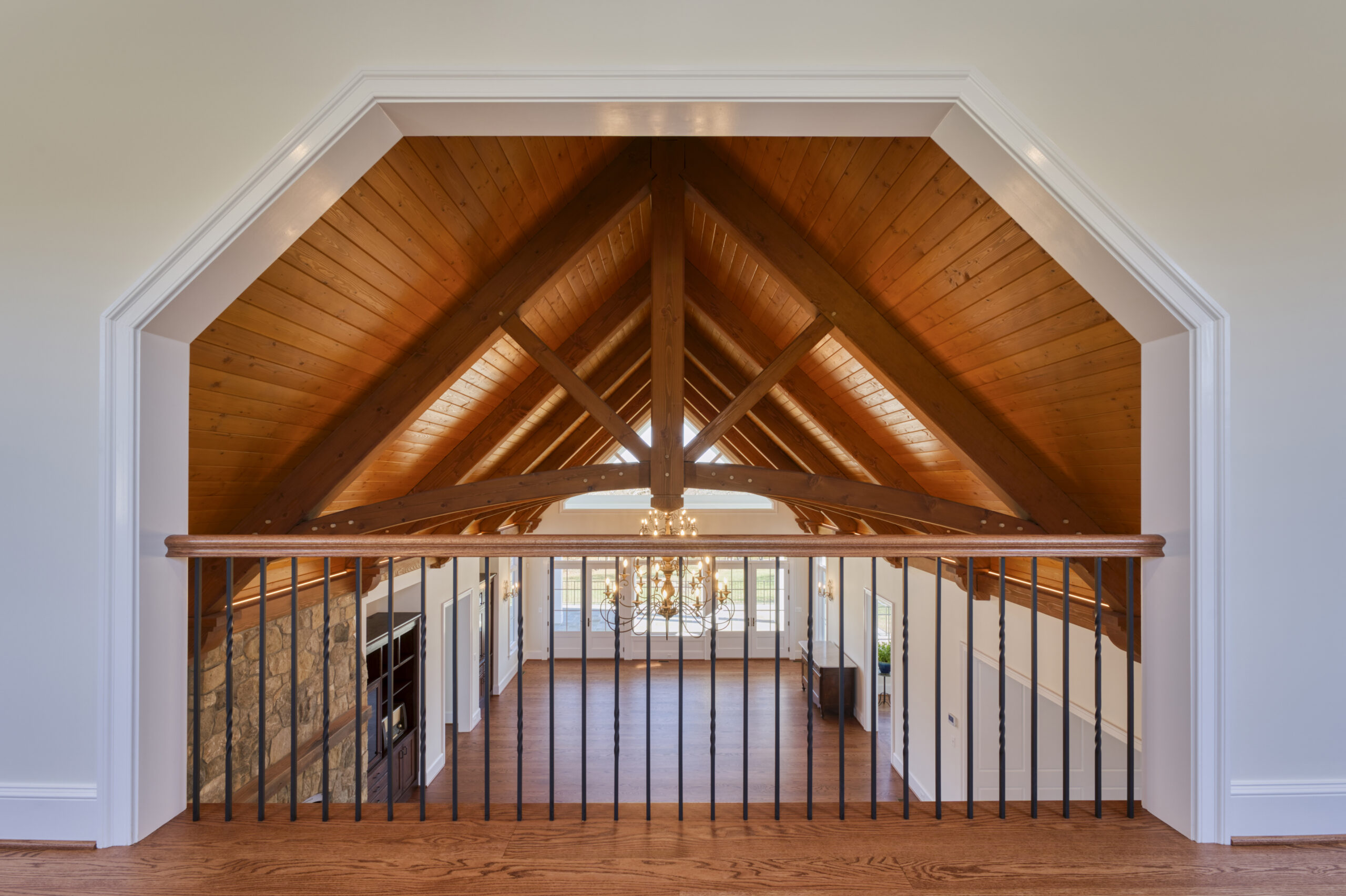 Professional interior photo of custom build new home by Black Oak Construction - showing the great room from the upper room overlooking, with hardwood floors, vaulted wooden ceiling with wooden trusses, stone fireplace and built-in cabinets on either side