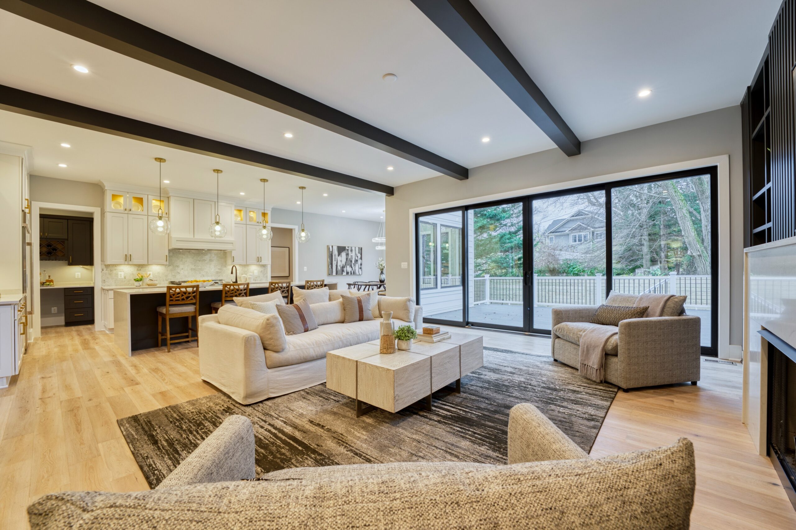 Professional interior photo of new construction home at 3400 N Ohio St - showing the open living room to kitchen with exposed black beams in the ceiling and a wall of floor to ceiling windows